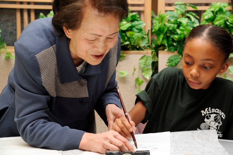 Setsu Yamamoto shows the daughter of Jessica Jones, Security Hill contractor, how to properly do brush art as she paints a flower during the 25th Annual Japan Day at Misawa Air Base, Japan, April 7, 2012. Brush art was one of the many cultural displays attendee's had the opportunity to take advantage of during the one-day event. (U.S. Air Force photo/Tech. Sgt. Marie Brown/Released) 
