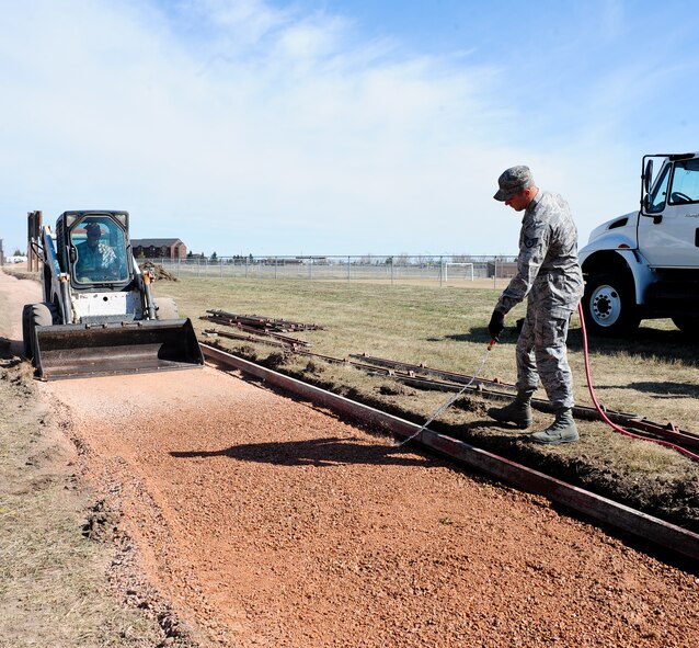 Staff Sgt. Kory Peterson, 28th Civil Engineer Squadron pavement and construction equipment technician, sprays down gravel with water during a sidewalk construction project at Ellsworth Air Force Base, S.D., April 4, 2012. Wetting the gravel makes it easier to compact and reduces the chances of cracking in the future.  (U.S. Air Force photo by Airman 1st Class Alystria Maurer/Released)