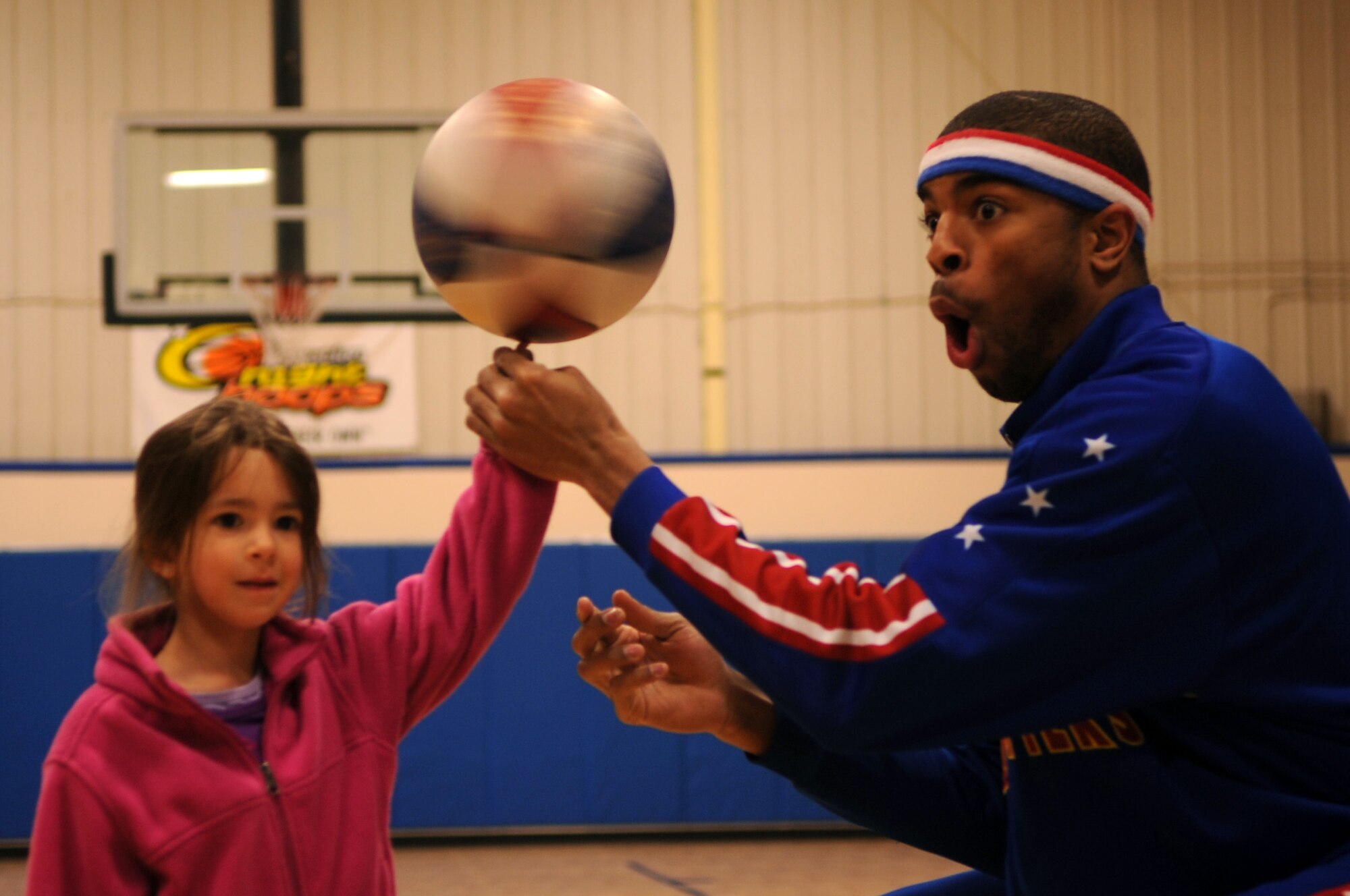 Harlem Globetrotter Hammer Harrison executes a basketball trick with a child at the Youth Center on Grand Forks Air Force Base, N.D., on April 9, 2012. Harrison came to GFAFB to motivate and educate children with the program “C.H.E.E.R. For Character” designed by the Globetrotters. This program helps children become better prepared for challenges they will face as young adults. (U.S. Air Force photo by Staff Sgt. Amanda Grabiec)