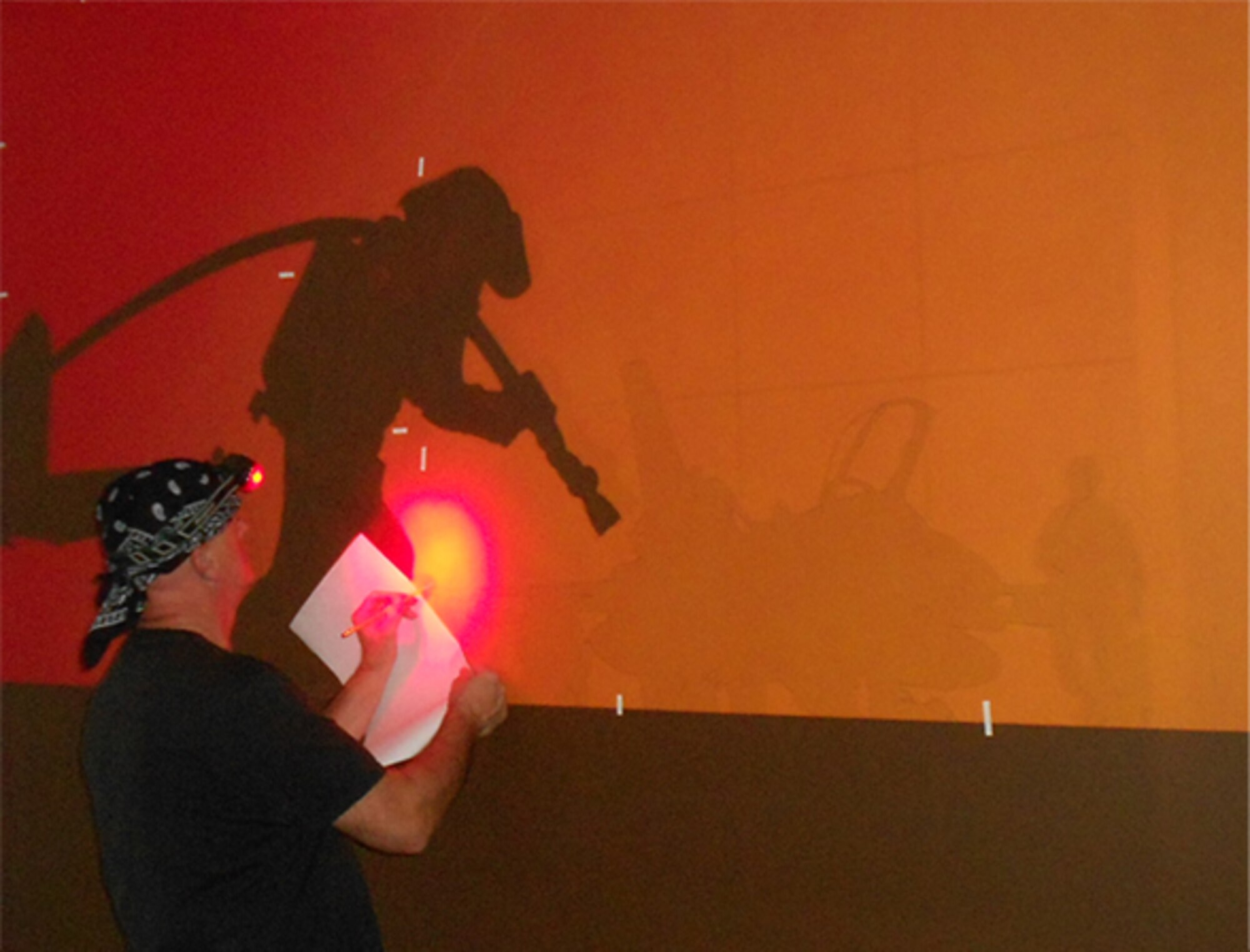 Dan Harman, Air Force Safety Center graphic artist and designer, uses a red LED headlamp to trace one of several projected images for a 153-square-foot mural in the Ground Safety Division conference room. Harman, who will retire April 30 with 23 years of federal service, was asked to create the mural as a visual reminder that ground safety impacts everyone, on and off duty. (U.S. Air Force photo by Lt. Col. Cindi Feldwisch)
