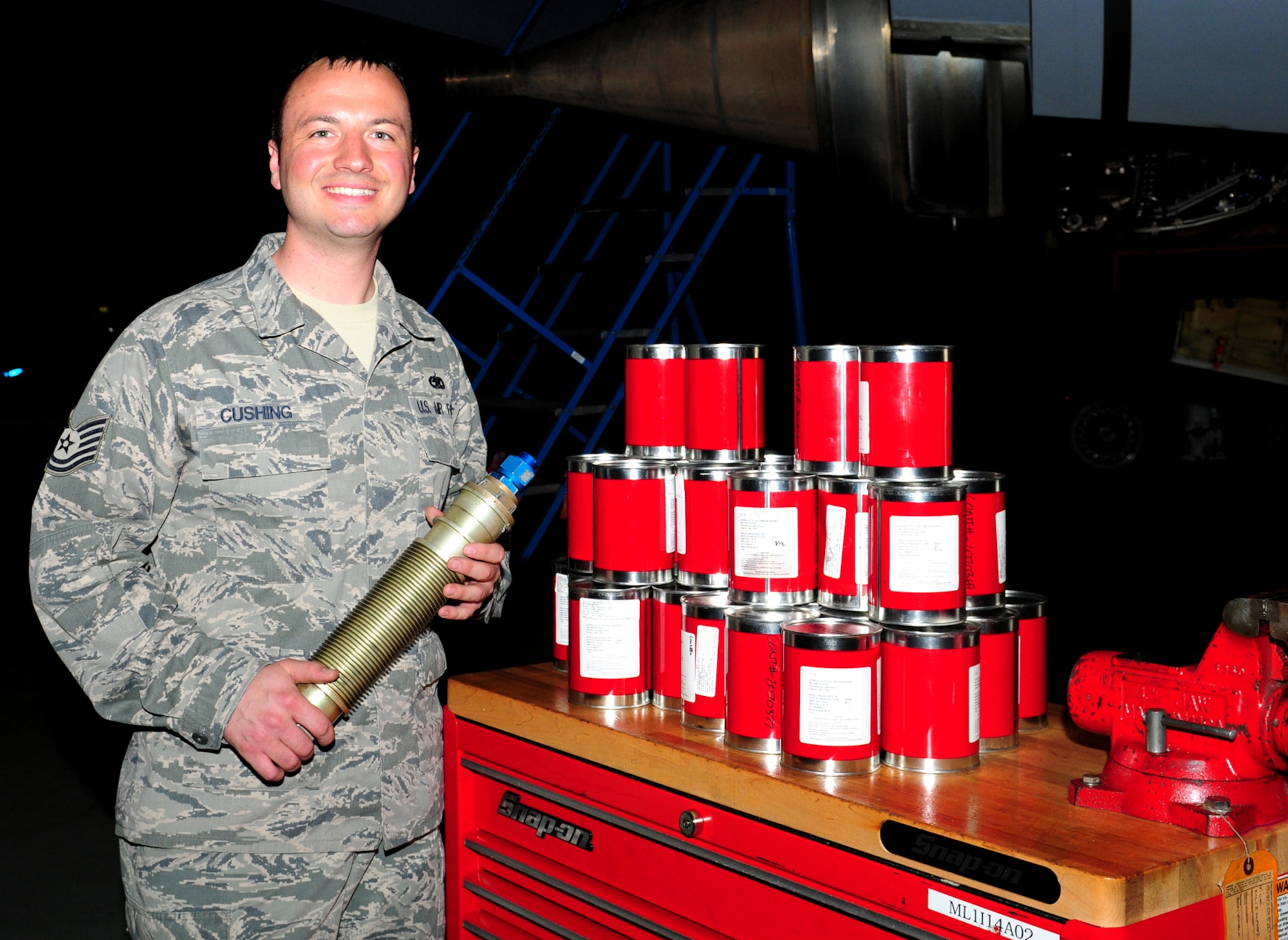 RAF MILDENHALL, England – Tech. Sgt. Blake Cushing, 100th Aircraft Maintenance Squadron flightline expeditor, poses with a hydraulic return filter assembly, and 36 quarts of hydraulic fluid. Cushing recently earned $10,000 through the Innovative Development through Employee Awareness program, after realizing it was not necessary to drain the reservoirs after every 900 flight-hour check when filters are changed. Until recently, during the inspection process the reservoirs were drained and 36 quarts of hydraulic fluid was replaced each time. The cans of hydraulic fluid shown above represent the amount saved during each inspection, through not having to drain the reservoirs. (U.S. Air Force photo/Karen Abeyasekere)