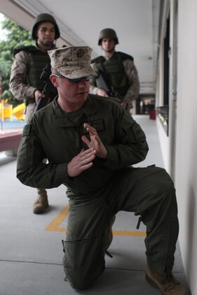 Sgt. Kyle Hill, a Provost Marshal’s Office Special Reaction Team leader, displays the proper technique for peeking around a corner on a knee to Lance Cpl. Jordan Barcon and Pfc. Edward Dix at the Matthew C. Perry School here April 10, 2012. Five candidates took part in the indoctrination brief, which included memorization drills, room-clearing exercises, step-out drills and weapon disassembly and reassembly.