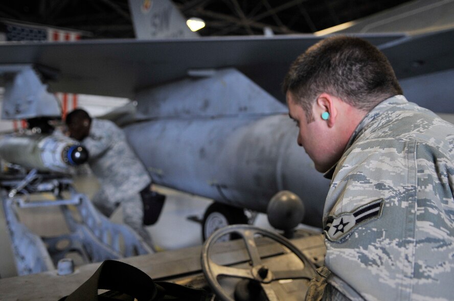 U.S. Air Force Airmen 1st Class T-Jay Queen, 77th Aircraft Maintenance Unit weapons specialist, watches Staff Sgt. Michael Johnson, 77th Aircraft Maintenance Unit weapons specialist, load a guided bomb unit onto an F-16 Fighting Falcon at Shaw Air Force Base, S.C., April 6, 2012.  These Airmen were competing in a quarterly load crew competition.(U.S. Air Force photo by Airman Nicole Sikorski/Released)