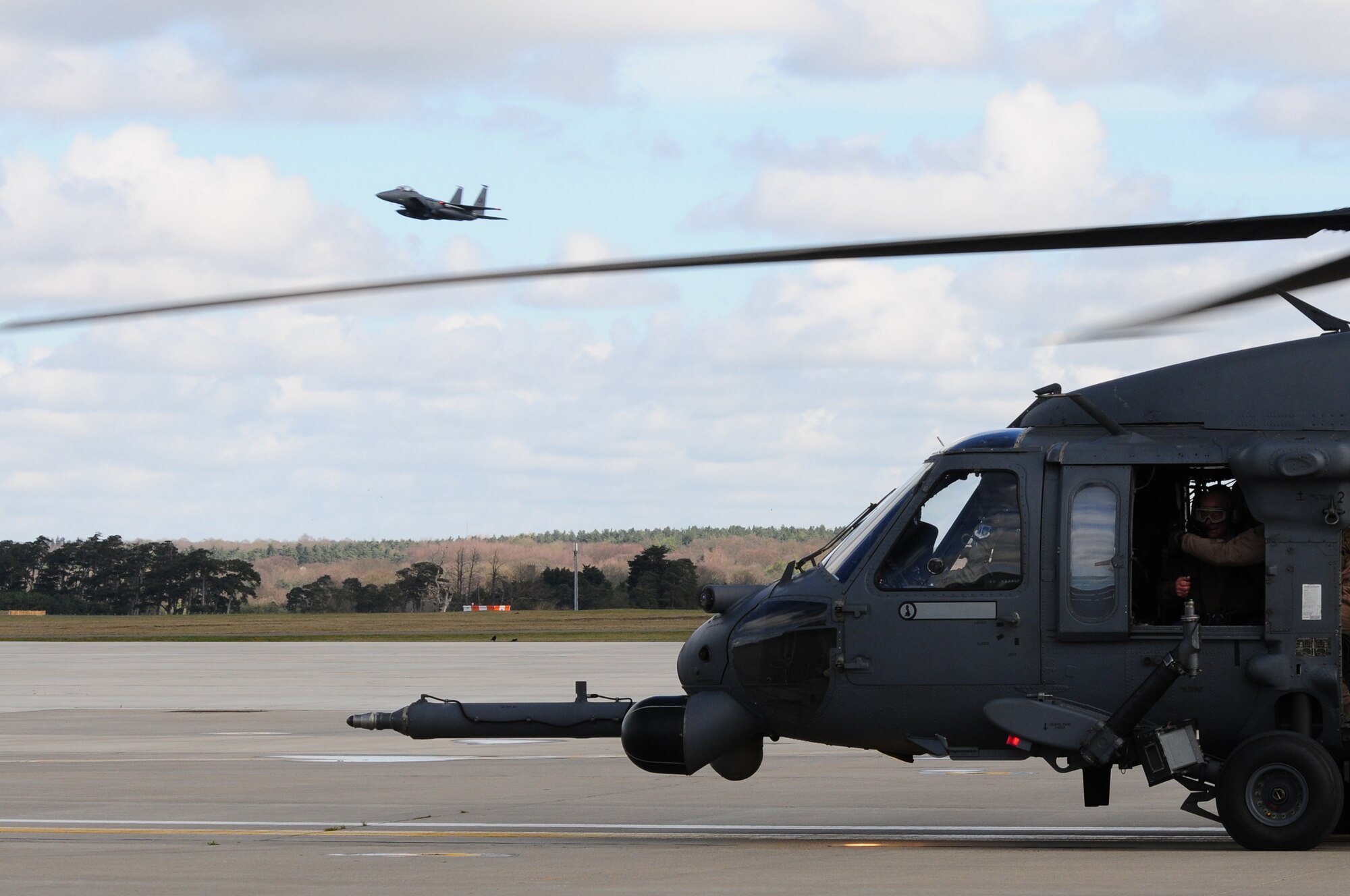 ROYAL AIR FORCE LAKENHEATH, England – An F-15E Strike Eagle flies by as retired Brig. Gen. Charles E. “Chuck” Yeager visits readies for his flight in an HH-60G Pave Hawk helicopter April 10, 2012.  Yeager visited the Liberty Wing to talk to Airmen about his Air Force career and experiences. (U.S. Air Force photo by Airman 1st Class Cory D. Payne)