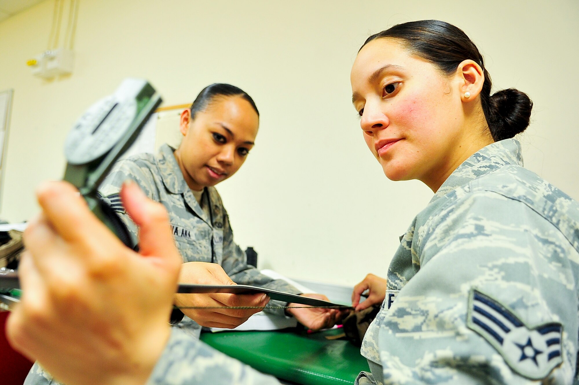 (Left) Staff Sgt. Chelsie Aiona Aka and Senior Airman Jennifer Lopez, both 51st Operations Support Squadron aircrew flight equipment journeymen, measure the length of a lanyard attached to a compass April 10, 2012. The length of the lanyard must be 60 inches long to ensure the compass can be read at eye level to accommodate the height of any pilot. (U.S. Air Force photo/Senior Airman Adam Grant)
