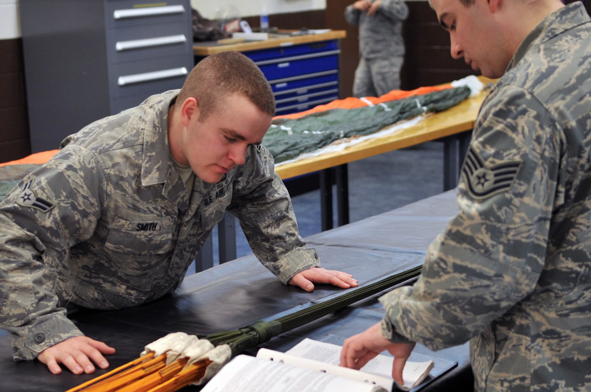 Airman 1st Class Taylor Smith and Staff Sgt. Anthony Sportsman, 51st Operations Support Squadron aircrew flight equipment journeymen, review technical orders to make certain every step is followed while inspecting a parachute here April 10, 2012. A technical order is a performance standard for specified processes that Airmen follow to perform their jobs. (U.S. Air Force photo/Staff Sgt. Craig Cisek)