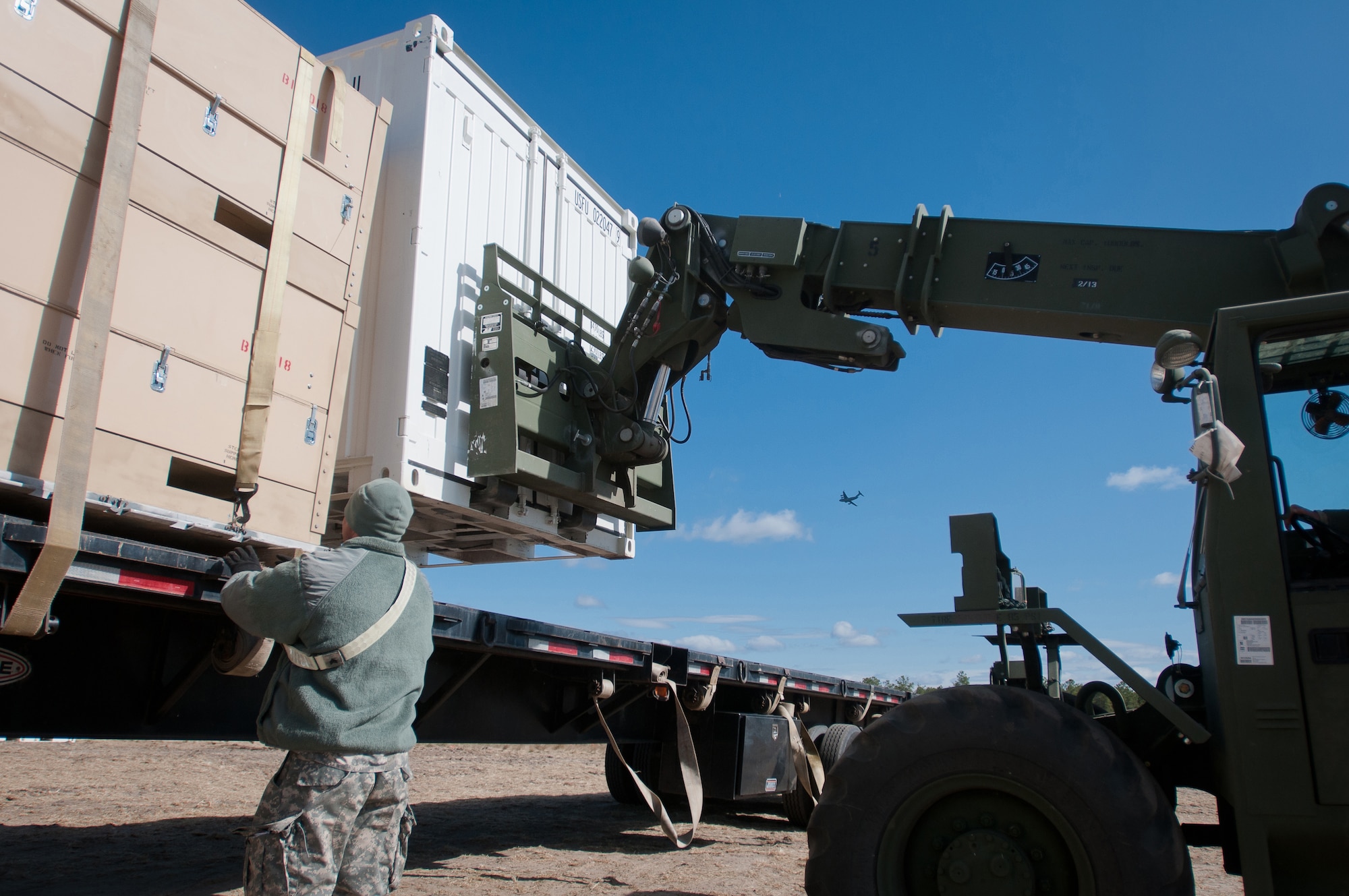 Army Sgt. Japheth Forehand, distribution NCO for the U.S. Army's 690th Rapid Port Opening Element in Fort Eustis, Va., secures a cargo container to a flatbed trailer as another is maneuvered into place and a C-17 flies overhead March 29, 2012, at Joint Base McGuire-Dix-Lakehurst, N.J. Forehand was working at the Forward Node of a Joint Task Force-Port Opening during Eagle Flag, a U.S. Air Force-sponsored exercise to prepare units for operating in deployed environments. The Kentucky Air National Guard's 123rd Contingency Response Group operated the airlift side of the JTF-PO, known as an Aerial Port of Debarkation. (U.S. Air Force photo by Maj. Dale Greer)
