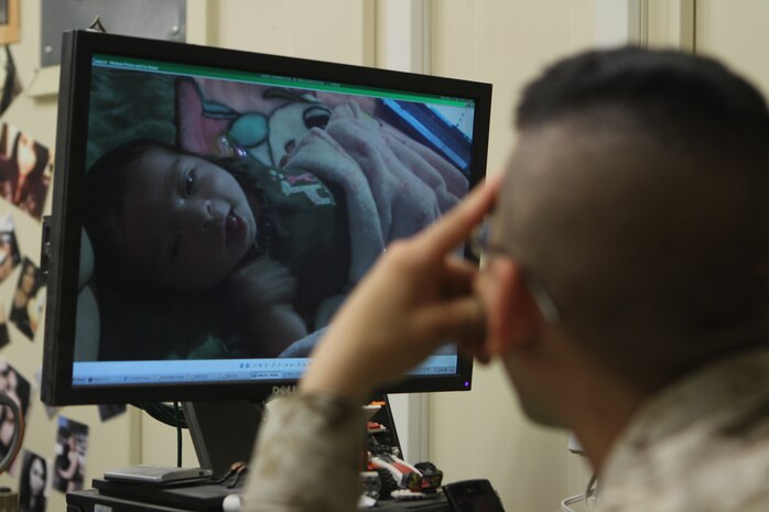 Lance Cpl. Juston Dickerson, supply administrator, Headquarters Battalion, 1st Marine Division (Forward), looks at pictures of his newborn daughter, Itzel. Dickerson video chats with his family every night, singing songs and reading stories to the child.