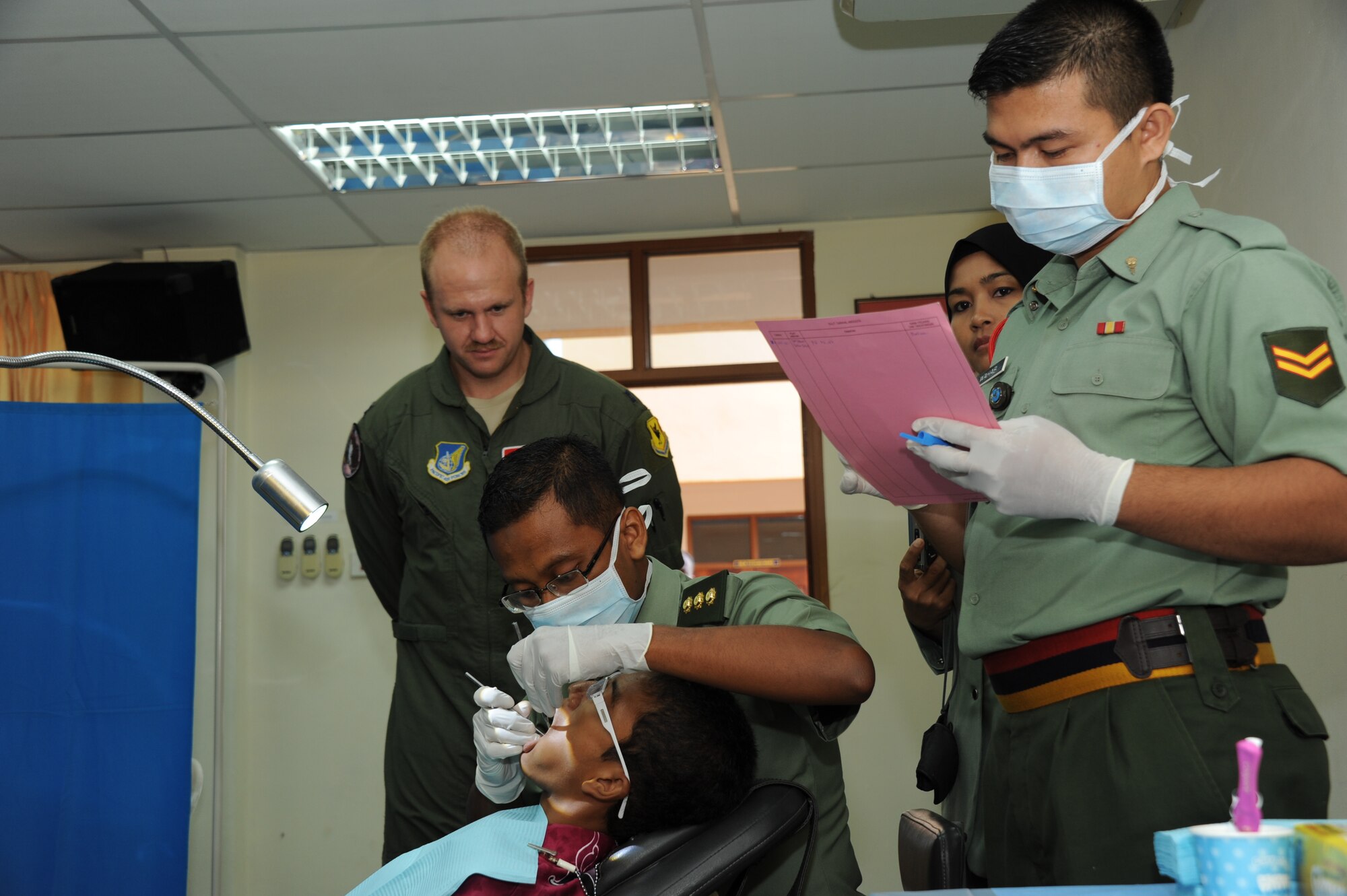 Capt. Brent Knudson (left), 67th Fighter Squadron flight surgeon, looks on as members of the Malaysian Army provide free dental service to an orphan at the Pertubuhan Pembangunan Anak-Anak Yatim Bekas Perajurit orphanage in Kulim, Malaysia, April 13, 2012. The day included not only free medical care, but a dedication ceremony for a multi-use sports court built by Royal Malaysian Air Force and U.S. Air Force airmen during Cope Taufan 2012. (U.S. Air Force photo/Master Sgt. Matt Summers)