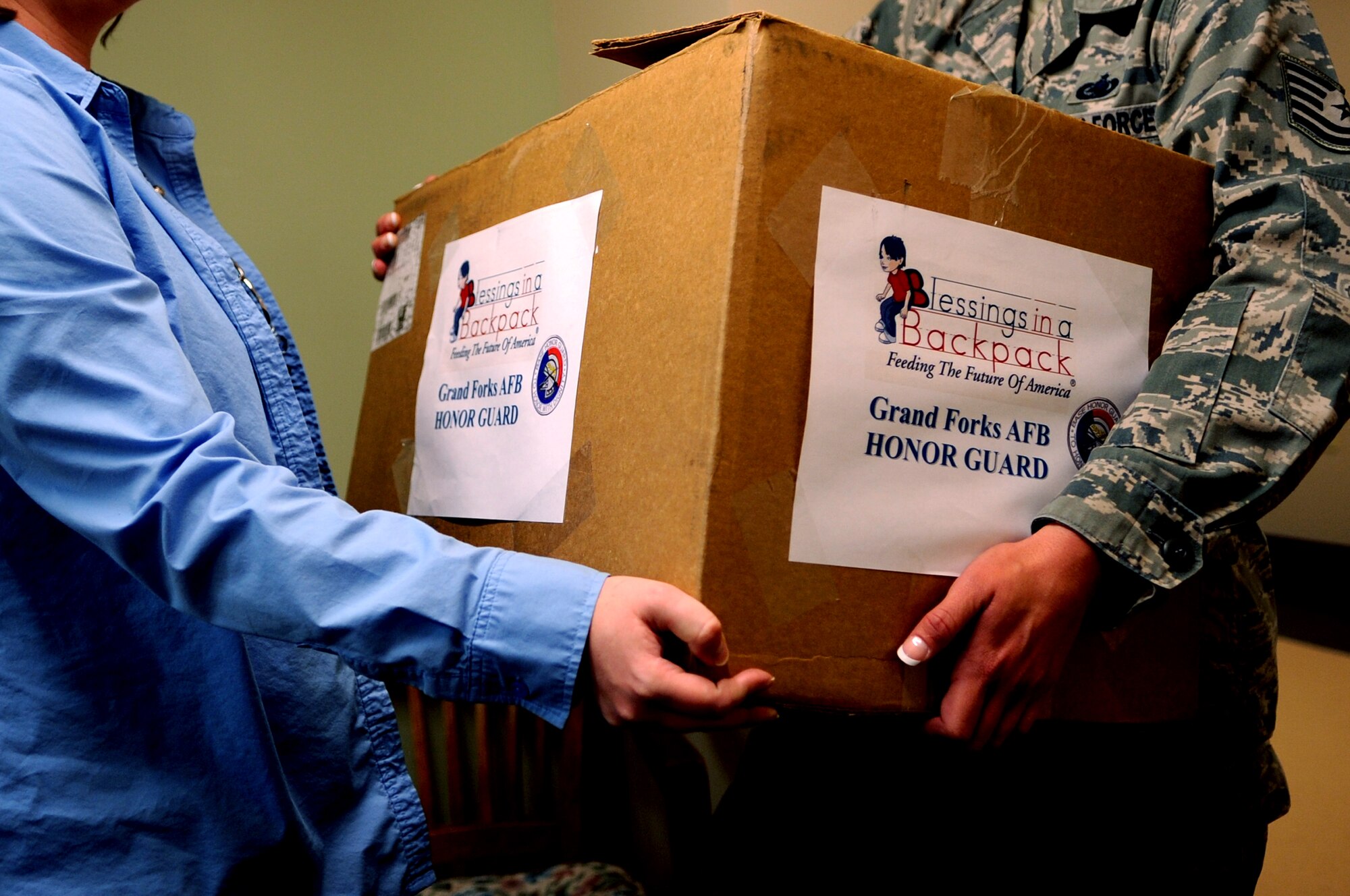 (From right) Tech. Sgt. Stephanie Rose, 319th Air Base Wing Honor Guard Program Manager from Grand Forks Air Force Base, N.D. , hands Laura McLaurin, a counselor at Sweetwater Elementary School in Devils Lake, N.D., a box filled with food on April 12, 2012. The Honor Guard has adopted the school and the food is meant to help feed children who all too often go hungry over the weekends.  (U.S. Air Force photo by Staff Sgt. Amanda N. Grabiec)