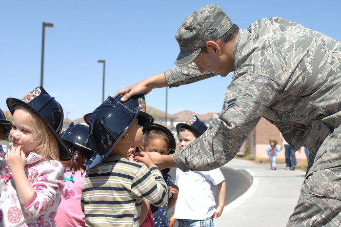U.S. Air Force Airman 1st Class Jake Cuevas, 99th Civil Engineer Squadron fire protection journeyman, helps children don their replica fire hats at the Child Development Center, April 10, 2012, at Nellis Air Force Base, Nev. Children learned about fire safety, fire drills, calling 911 and other emergency procedures during the visit. (U.S. Air Force photo by Senior Airman Jack Sanders)  