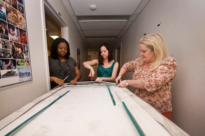 Takeira Jones-Bolden, 99th Force Support Squadron marketing assistant, Christina Hilliard, 99th FSS marketing specialist, and Kate Berry, 99th FSS Director of Marketing, unwrap foam board April 17, 2012, at Nellis Air Force Base, Nev. The new foam board, used for various marketing products, is made of recycled and re-purposed materials. (U.S. Air Force photo by Staff Sgt. Christopher Hubenthal)