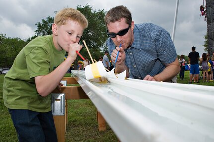 Ray Quenneville, 902nd Comptroller Squadron, and his son, Kyle, use straws to blow their boats across the finish line April 14 at Joint Base San Antonio-Randolph, Texas. Famaganza is a yearly family celebration that includes performances, games, prizes and a book fair. (U.S. Air Force photo by Benjamin Faske)