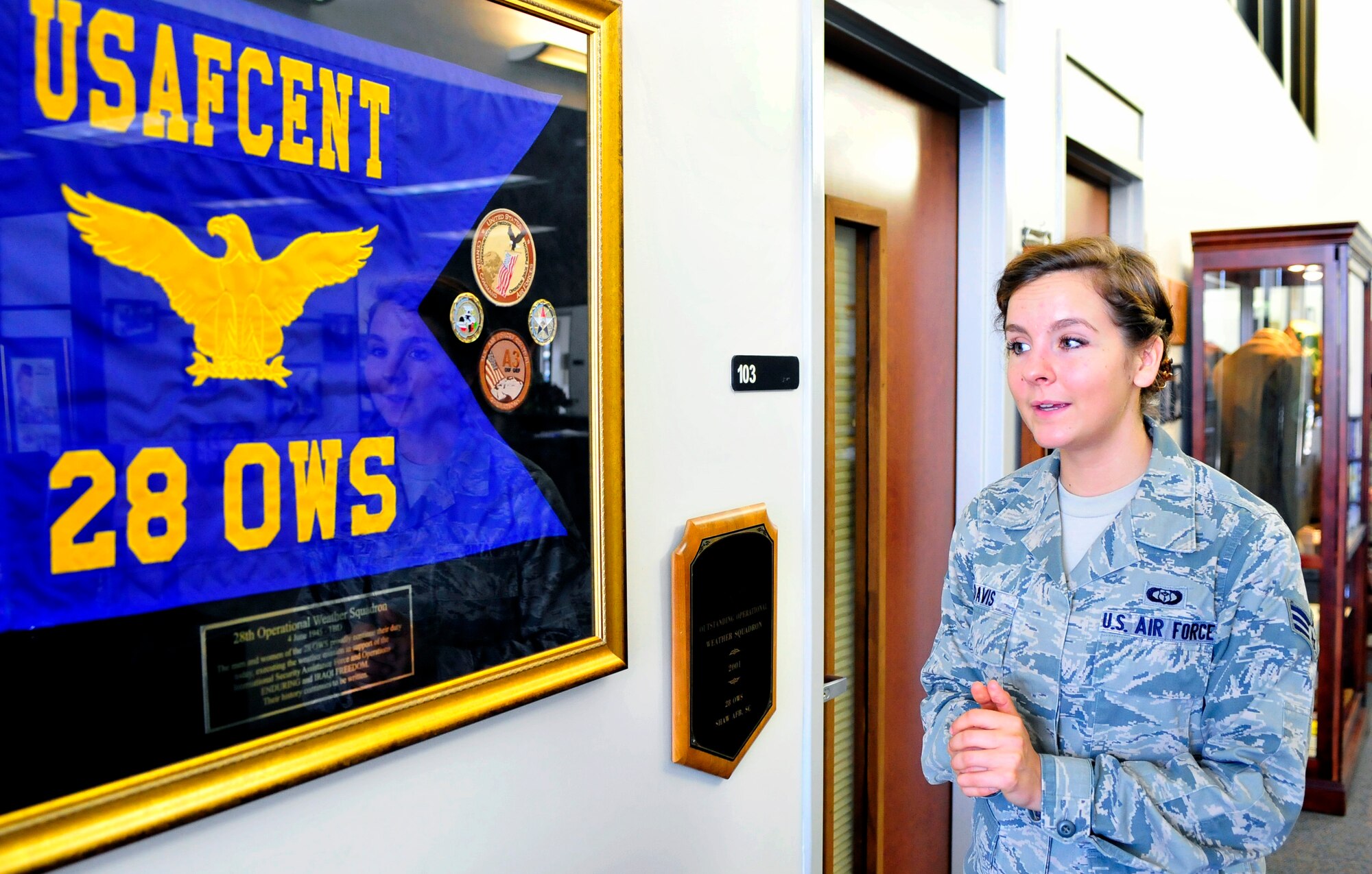 Senior Airman Rachel Davis, 28th Operational Weather Squadron forecaster, gives a brief history of the squadron by a guide-on flag and some squadron memorabilia in the 28th OWS lobby, Shaw Air Force Base, S.C., April 6, 2012. Volunteers from the 28th OWS created an Air Force memorabilia display in their lobby to help squadron members and visitors gain a sense of pride in their heritage. (U.S. Air Force photo by Senior Airman Daniel Phelps/Released)