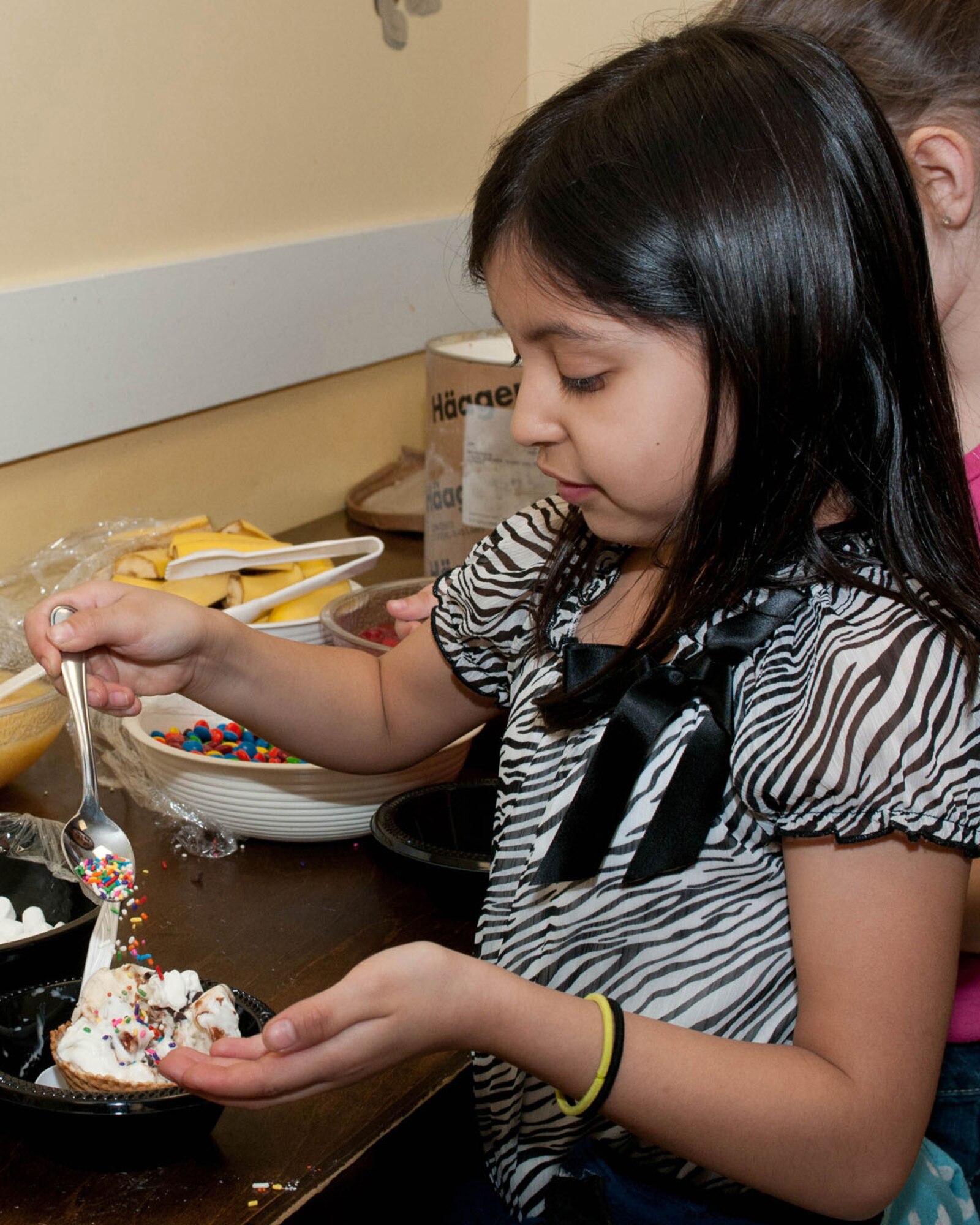 HANSCOM AIR FORCE BASE, Mass. - Jirvani Perez sprinkles a sundae her way during an ice cream social April 11 in the clubhouse at the School Age Program building. The ice cream social is just one of many events held throughout the base to celebration Month of the Military Child. (U.S. photo by Linda LaBonte Britt)