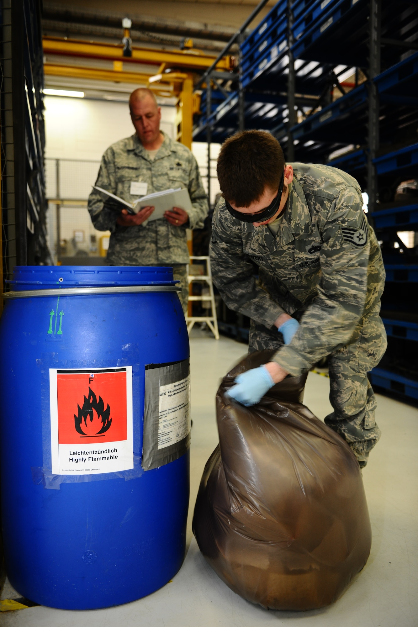 SPANGDAHLEM AIR BASE, Germany – Staff Sgt. Dustin Majewski, 52nd Component Maintenance Squadron propulsion support technician, empties a hazardous waste container while Master Sgt. Chad Haughenbury, U.S. Air Forces in Europe hazardous materials manager, inspects the work center during an Environmental, Safety and Occupational Health Compliance Assessment Management Program evaluation inside the jet propulsion maintenance shop here April 18. The week-long ESOHCAMP assessment gives the base an idea of how its compares to U. S. Air Force and host-nation regulations regarding environmental and occupational safety. This team is made up of 15 USAFE evaluators who assess Spangdahlem AB’s overall health. The base uses the results from the program to help become USAFE’s most environmentally friendly wing. (U.S. Air Force photo by Airman 1st Class Dillon Davis/Released)