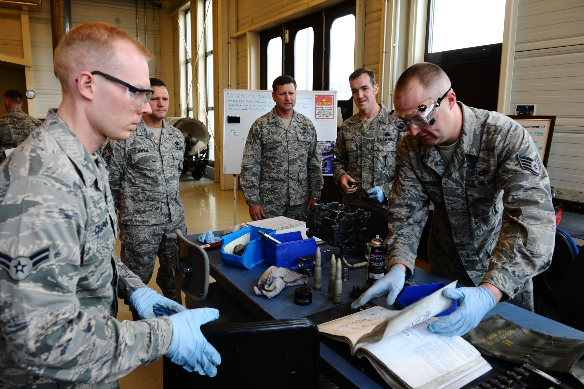SPANGDAHLEM AIR BASE, Germany – Airman 1st Class Nicholas Chapman, left, and Staff Sgt. Michael Stephens, right, 52nd Equipment Maintenance Squadron ammunition specialists, use a technical order to take apart and reassemble an F-16 Fighting Falcon ammunition loader while Chief Master Sgt. Oscar Mackin, 2nd Air Force command chief, and Maj. Gen. Leonard Patrick, 2nd AF commander, tour 372nd Training Squadron Detachment 2 classrooms and training facilities inside Bldg. 43 here April 18. Patrick and Mackin visited the 372nd TRS Det 2 during their 2nd AF overseas units tour. The detachment offers advanced skills using classroom and hands-on training on the F-16 Fighting Falcon and A-10 Thunderbolt II for more than eight different aircraft maintenance career fields. (U.S. Air Force photo by Airman 1st Class Dillon Davis/Released)