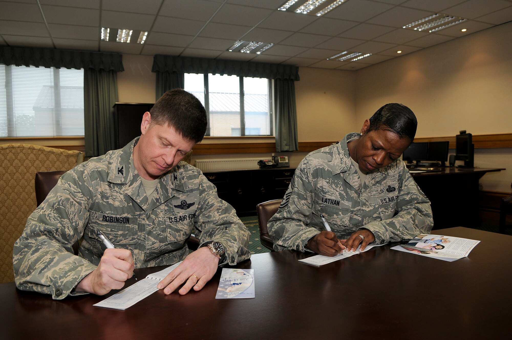 ROYAL AIR FORCE LAKENHEATH, England -- Col. Kyle Robinson, 48th Fighter Wing commander, and Chief Master Sgt. SaRita Lathan, 48th FW command chief, sign contributions to the 2012 Air Force Assistance Fund on April 18, 2012. Contributions to the campaign support the Air Force Aid Society, Air Force Enlisted Village, Air Force Village and the General and Mrs. Curtis E. LeMay Foundation.  (U.S. Air Force photo by Staff Sgt. Connor Estes)
