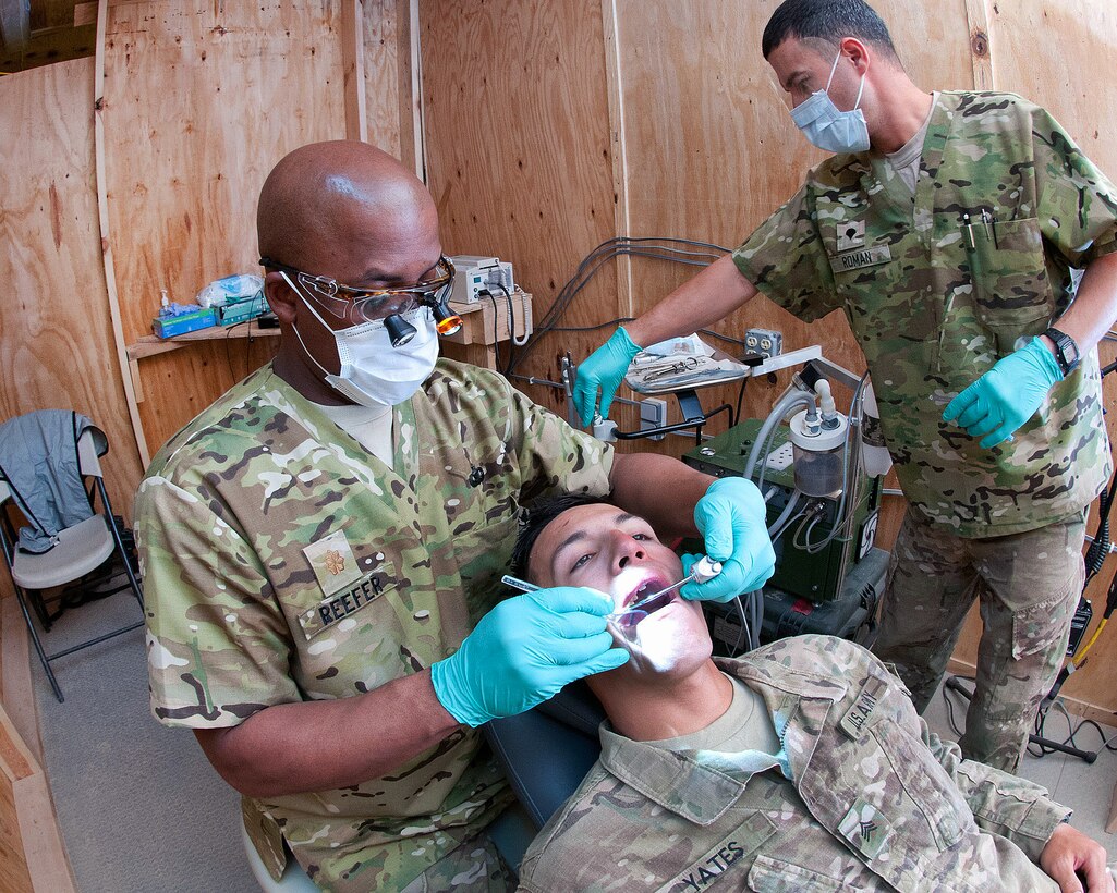 U.S. Army Maj. Murray Reefer, left, aerates U.S. Army Sgt. Preston Yates' tooth as he prepares to fill a cavity with the assistances of U.S. Army Spc. Francisco Roman, right, on Forward Operating Base Arian in Afghanistan's Ghazni province, April 17, 2012. Reefer, a dentist, Roman, a dental hygienist, and Yates are assigned to the 82nd Airborne Division’s 1st Brigade Combat Team.