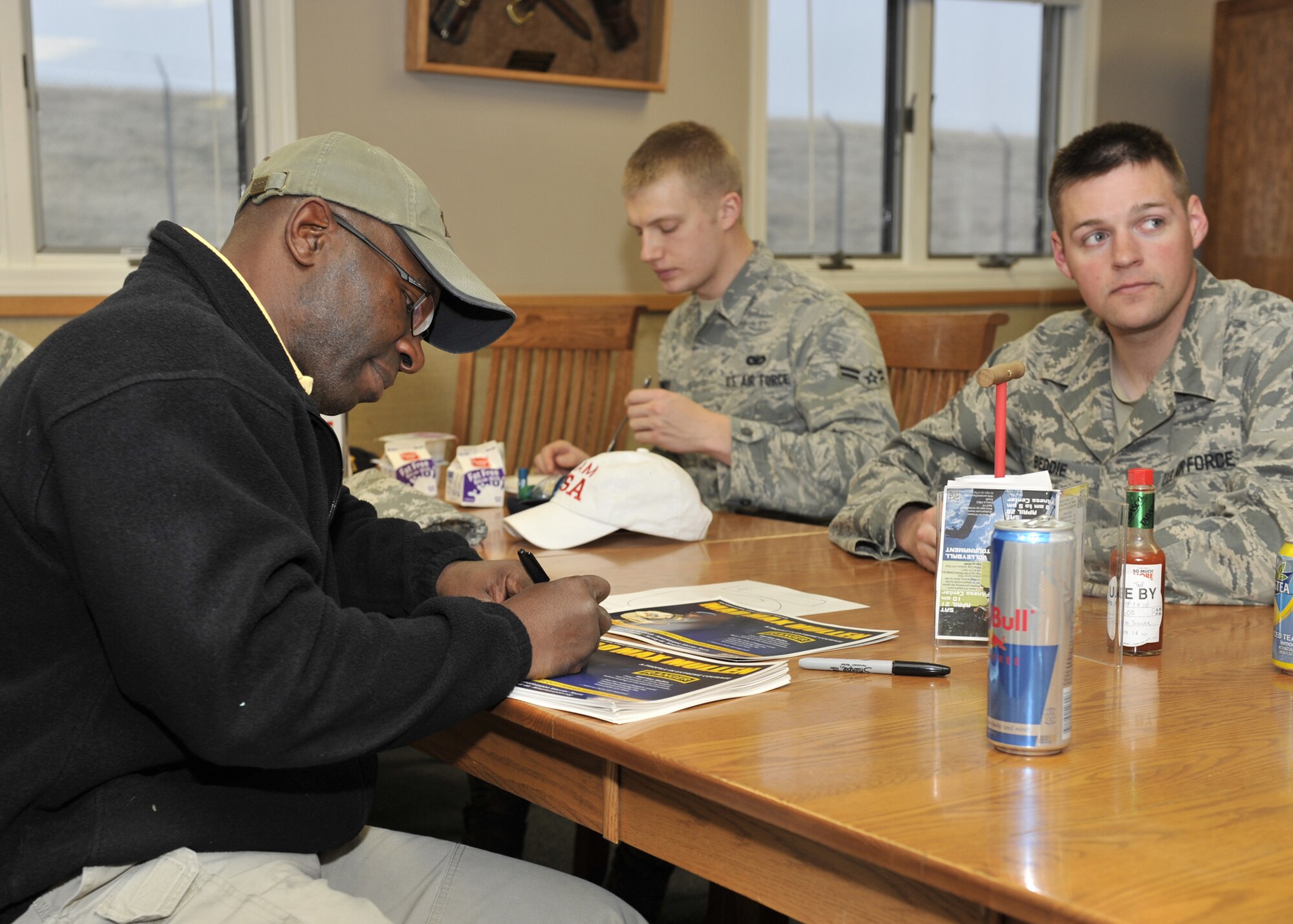U.S. Army retired Master Sgt. Howard "Mad Max" Mullen autographs pictures for members in the missile field as Airman 1st Class Kevin Kennedy and Senior Airman Philip Beddie, 341st Missile Wing Security Forces Squadron members, finish breakfast. Mullen shared the challenges and accomplishments he had serving as a U.S. Army Ranger, hoping to promote determination in security forces Airmen. (U.S. Air Force photo/John Turner)