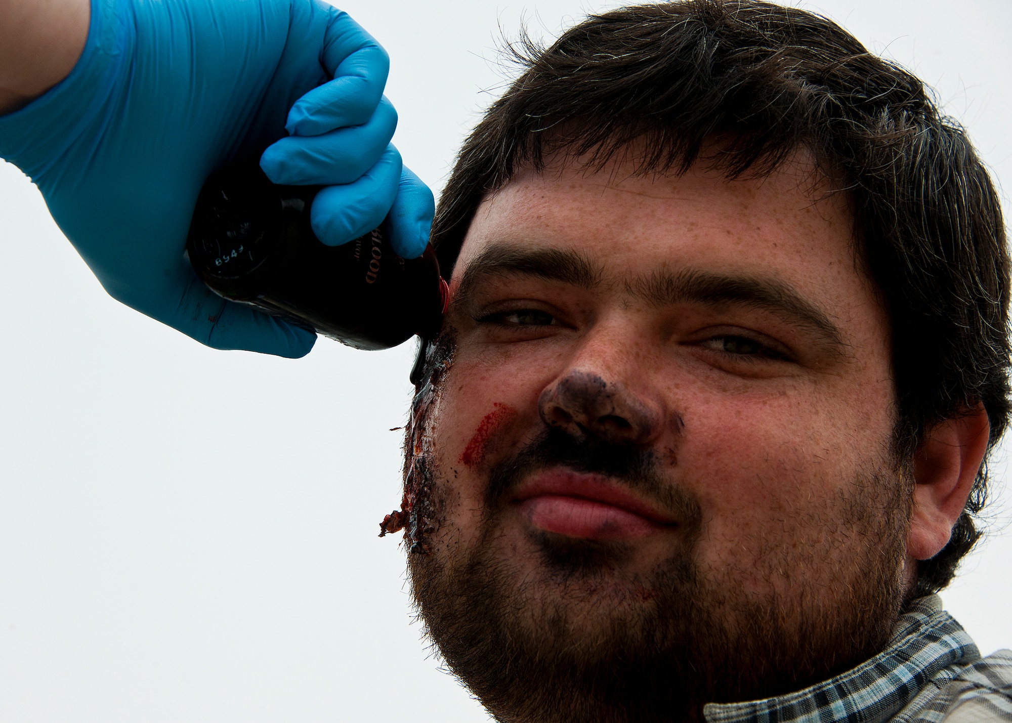 A 96th Medical Group moulage team member applies more blood to a victim's face prior to the mass casualty exercise April 19. The moulage team turned more than 40 volunteers into ‘horror movie’ realistic victims of an aircraft fire.  The team’s “art” provides a sense of realism in exercises that medics and first responders may encounter in real-world accidents.  (U.S. Air Force photo/Samuel King Jr.)