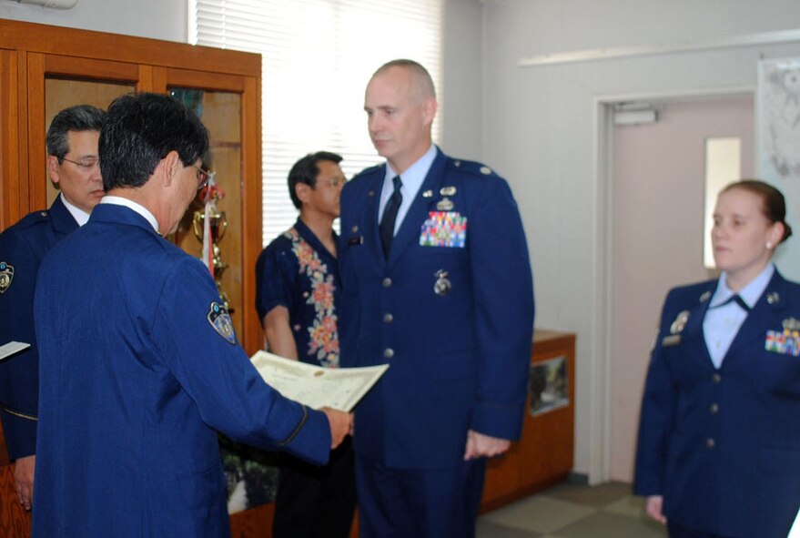 Chief Tatsuhiko Toguchi, Okinawa Prefectural Police Okinawa Police Station chief, presents a letter of appreciation to U.S. Air Force Lt. Col. John Grimm, 18th Security Forces Squadron commander, April 18, 2012, in Okinawa, Japan. Grimm and U.S. Air Force Tech. Sgt. Shannon Williams, 18th SFS NCO in charge of investigations (right), were presented letters and mementos for their contributions toward fostering the 18th SFS and Okinawa Police relationship. (Courtesy photo)