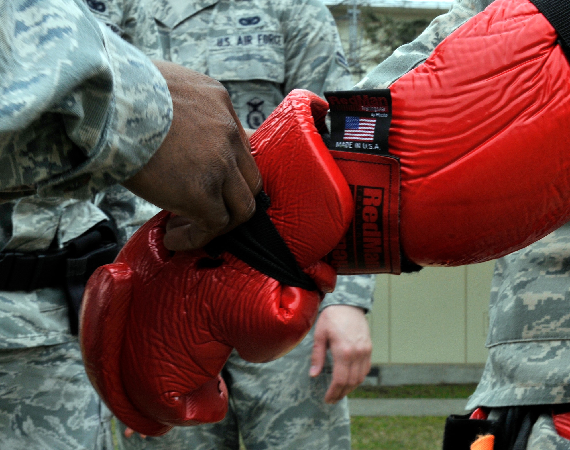 U.S. Air Force Staff Sgt. James Jackson tightens the strap of a protective glove on Senior Airman Brian Childress during baton training April 19, 2012 at Misawa Air Base, Japan. Baton training, also known as red man training, gets its name from the large red suit Airmen wear as they portray an assailant. Both Airmen are 35th Security Forces Squadron patrolmen. (U.S. Air Force photo by Tech. Sgt. Phillip Butterfield/Released) 