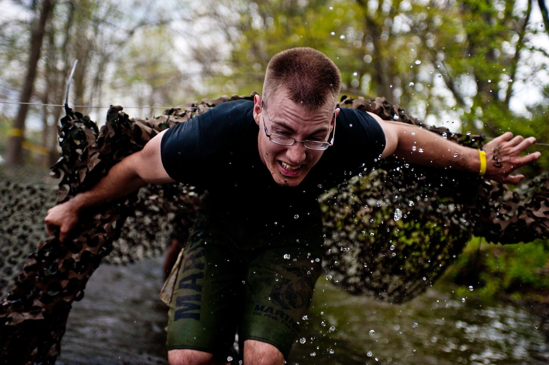 Lance Cpl. Alex Robinson, Guard Company Marine, exits a camouflage net tunnel in a river during the Civilian Military Combine at Bryce Resort, Va., April 21, 2012. The Combine, a weight lifting competition followed by a mountainous 6-mile obstacle course, was the fourth event in the 2012 Commander's Cup series. While Robinson was not part of the Marine Drum & Bugle Corps' team, he ran with them for the majority of the course.