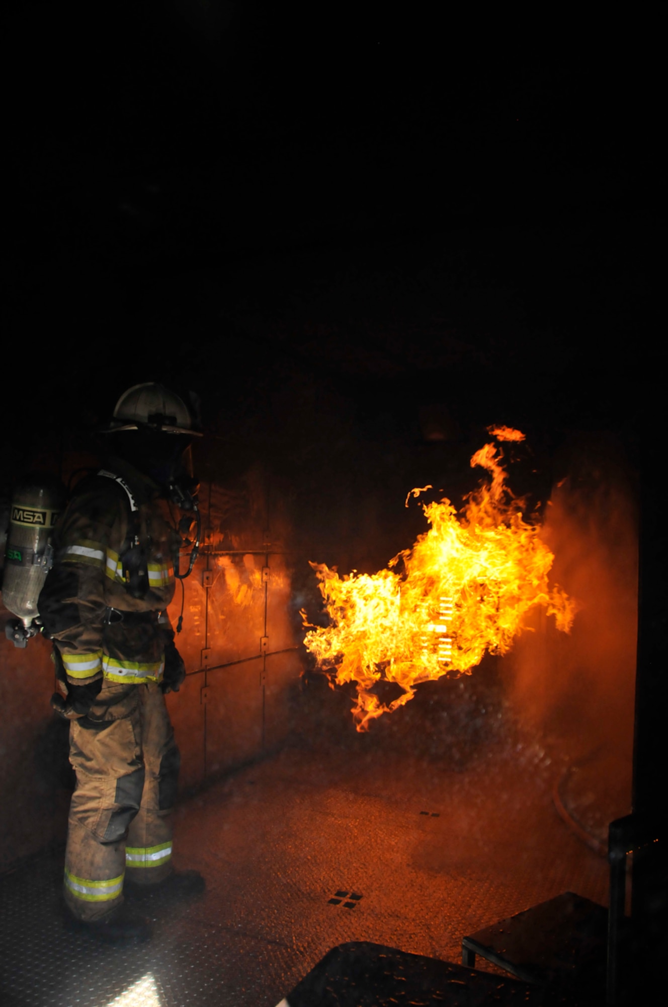 An AEDC firefighter monitors a fire in the bottom floor of West Virginia University Fire Service Extension’s training trailer as his crewmates come down from the second floor of the unit. Two floors of the trailer allows firefighters to simulate going up stairs into attics and into basements to battle fires. (Photo by Rick Goodfriend)
