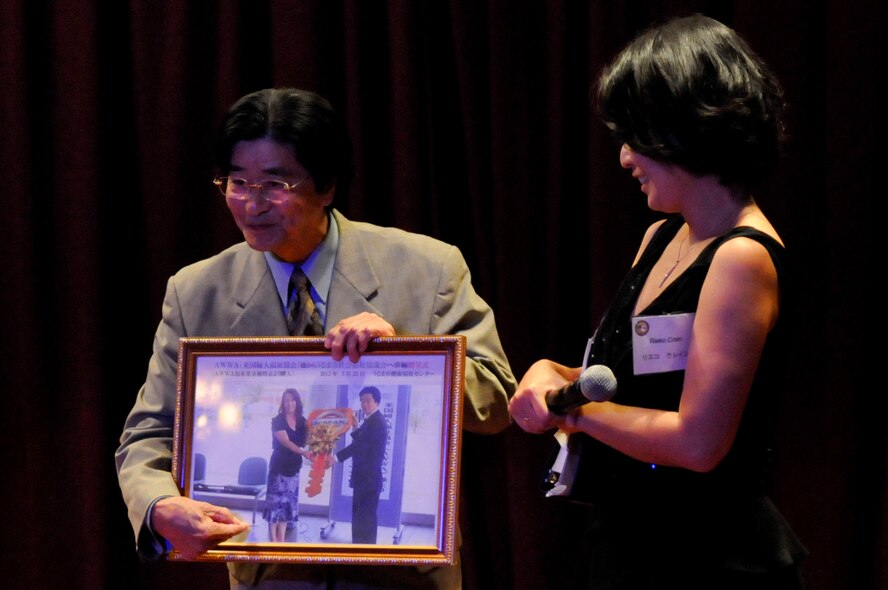 Kenkou Nakayama, Uruma City Welfare Councilman, describes a picture of a giant key representing a wheelchair-accessible van donated to his elderly care facility by the American Women's Welfare Association during the 2012 AWWA Friendship Social at Kadena Air Base, Japan, April 23, 2012. The social marked the 40th anniversary of the AWWA and recognized more than $7 million in donations to Japanese charities and American organizations over the years. (U.S. Air Force photo by Airman Tara A. Williamson/Released)