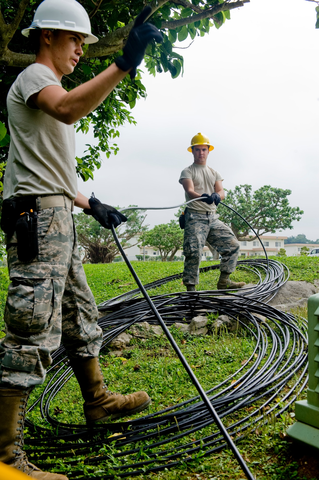 U.S. Air Force Airman 1st Class Brandon Courtain-Tharp and Airman 1st Class Tanner Audia, 18th Communications Squadron (CS) cable systems journeyman, pull fiber optic cable from a manhole on Kadena Air Base, Japan, April 24, 2012. The cable will reach three schools as well as the administration building on Kadena. (U.S. Air Force photo by Airman 1st Class Hailey R. Davis/Released)