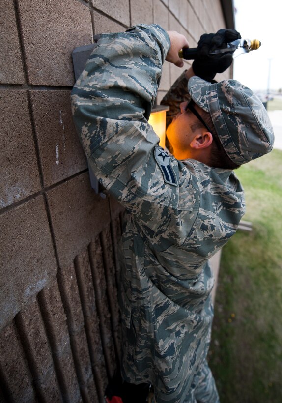 Airman 1st Class Alex Price, 28th Civil Engineer Squadron electrical systems technician, loosen a security light case during while replacing a light bulb on a maintenance building near the flightline at Ellsworth Air Force Base, S.D., April 20, 2012. Many of the security lights necessary for night operations, were not working properly and needed to be replaced. (U.S. Air Force photo by Airman 1st Class Alystria Maurer/Released)
