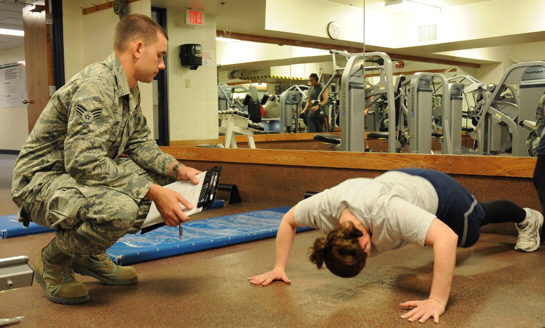 Senior Airman Chris Dye, 28th Maintenance Squadron avionics test station component journeyman, supervises Staff Sgt. Wanda Carr, 28th Logistics Readiness Squadron training manager, during the push-up portion of the physical fitness test at the Bellamy Fitness Center at Ellsworth Air Force Base, S.D., April 24, 2012. Due to recent changes in the physical fitness testing program, military physical training leaders from each squadron will now be administering the physical fitness test. (U.S. Air Force photo by Airman 1st Class Anania Tekurio/Released))