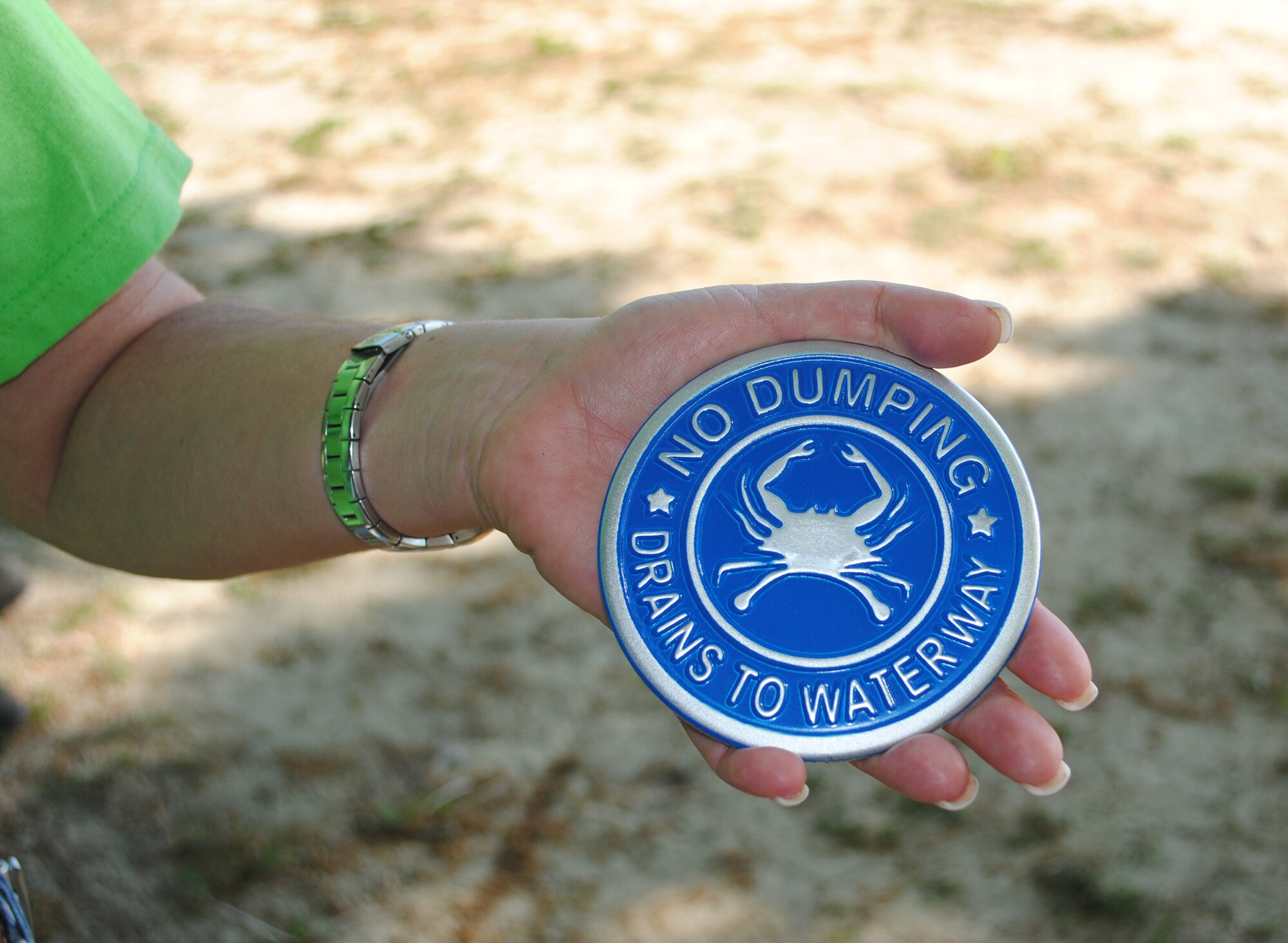 Susan Miller, Civil Engineer Division Environmental Element chief, 733rd Civil Engineer Division, holds a medallion that volunteers affixed near sewer lines to remind people to stay away from dumping in the drains. Miller was part of a group of nearly 45 volunteers who came together April 16 to kick off Joint Base Langley-Eustis’ Earth Day activities. (Courtesy photo by Toni Guagenti/Released)