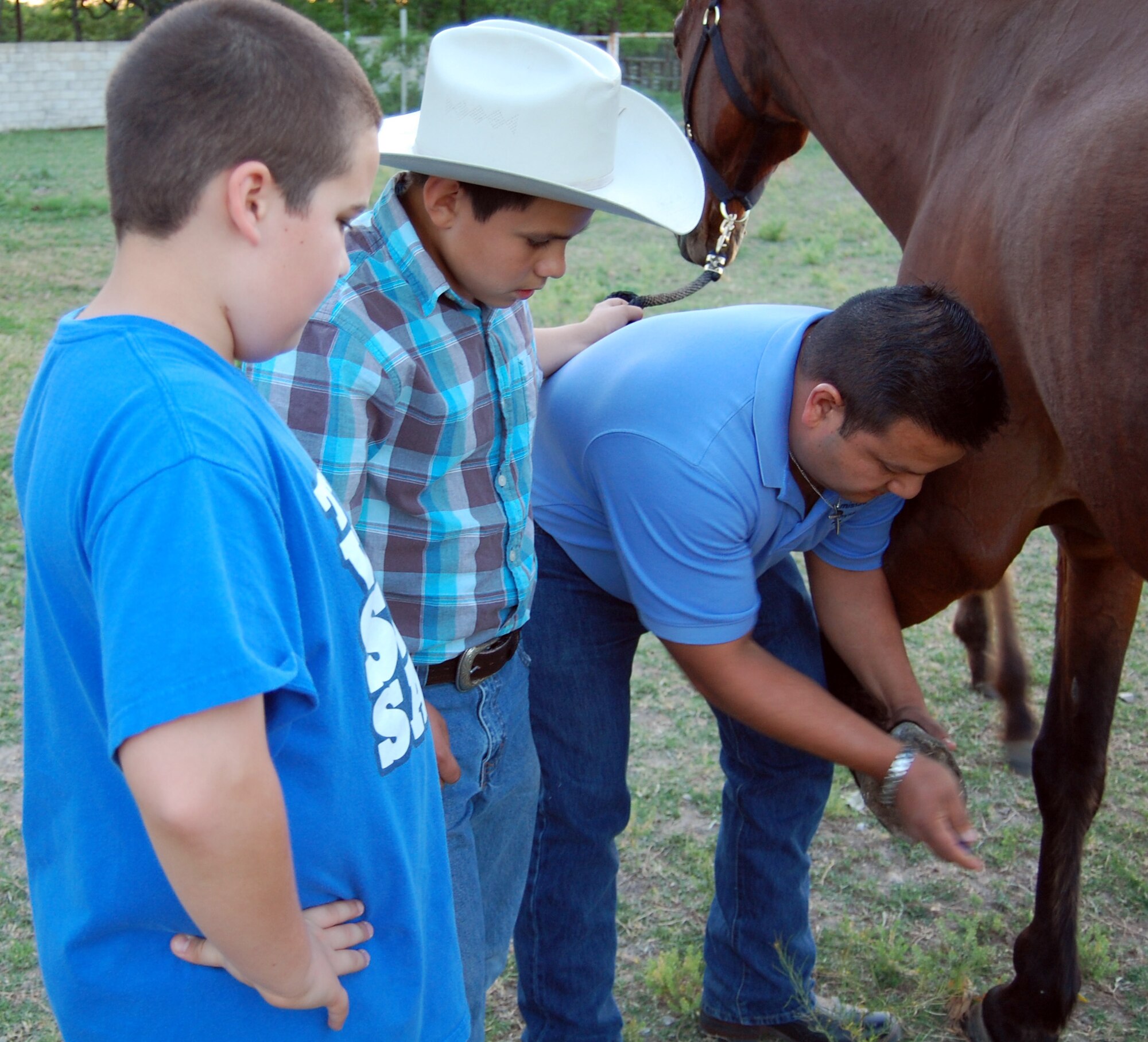 Memo Montejano, an Amistad Physical Therapy technician, demonstrates how to clean out the hooves of a horse to his son Memo Jr. and Joshua Waid, at the Waid family home in Del Rio, Texas, April 17, 2012. Montejano and his son are 12-time successful horse rescuers and the Waid family is helping them care for a rescue horse at their residence. (U.S. Air Force photo/Jack Waid)
