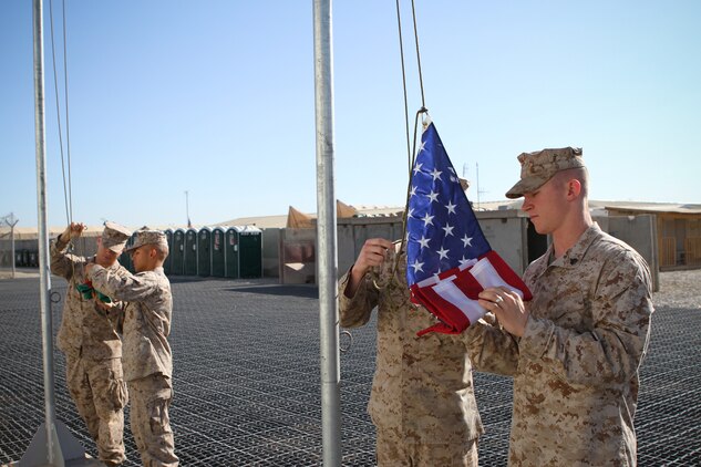 Sergeant Bryce W. Cherryholmsnoll, a native of Huxley, Iowa, unfolds the American flag as Marines prepare to fly the flag next to the Afghan flag above the Task Force Leatherneck compound here April 28, 2012. Marines serving here have the opportunity to fly a 3-by-5-foot American flag for a day and dedicate it to someone of their choice.
