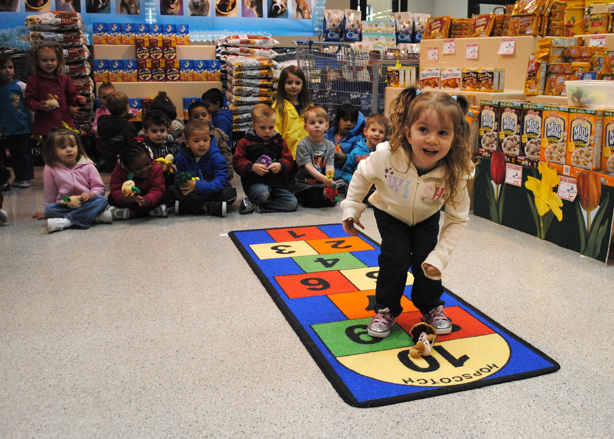 Ella Bradley, 4, is all smiles as she plays a game of hopscotch at the Commissary April 20. Children from the Child Development Center played games that tested their vegetable knowledge, made fruit kabobs and listened to Tech. Sgt. Gabriel Carbajal, 341st Medical Operations Squadron NCO in charge of the Health and Wellness Center, talk about healthy eating. The HAWC participated in educating members of the CDC in support of the Month of the Military Child, a month to recognize the role of military children. (U.S. Air Force photo/Airman 1st Class Katrina Heikkinen)