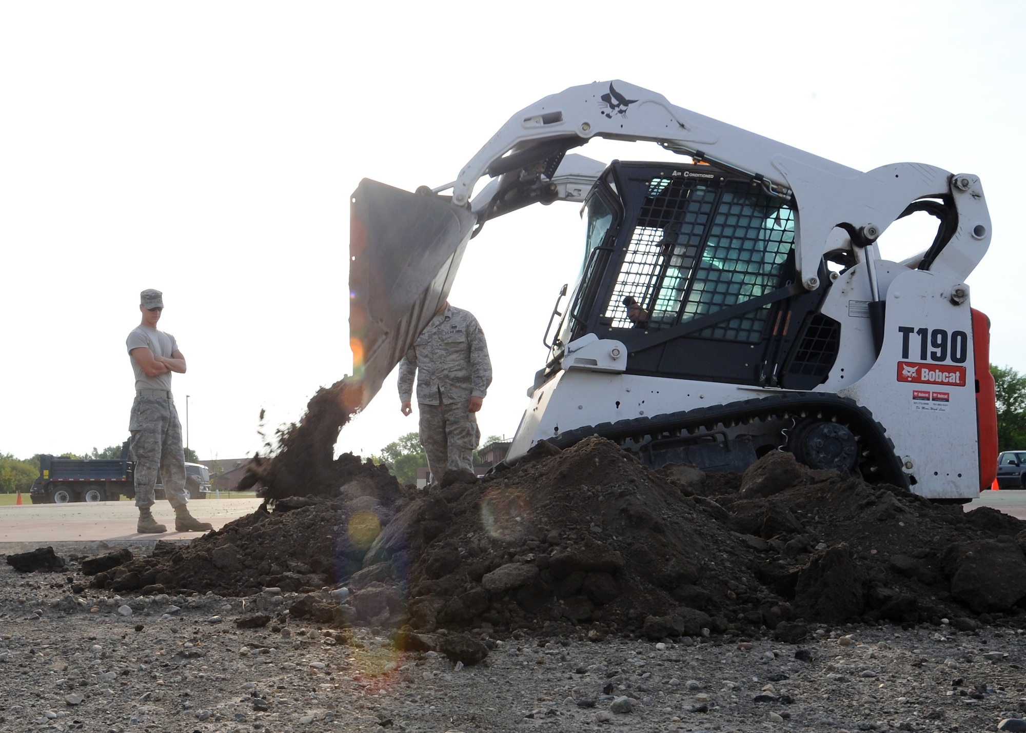 Members of the 319th Civil Engineer Squadron use a compact track loader to plow dirt for a cement block on July 23, 2012, on Grand Forks Air Force Base, N.D.  The block will hold the flag pole for a new drill pad.  (U.S. Air Force photo by Airman 1st Class Xavier Navarro)