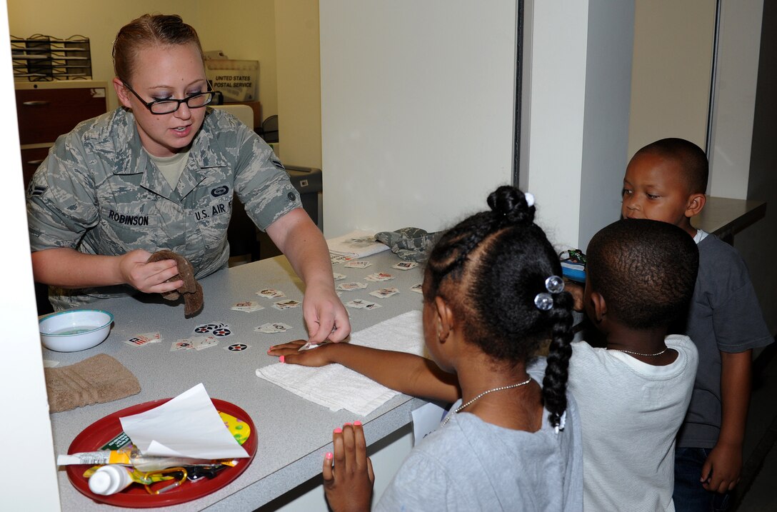 U.S. Air Force Airman 1st Class Haeley Robinson, 30th Intelligence Squadron geospacial intelligence analyst, gives children temporary tattoos during Operation Hero, at Langley Air Force Base, Va., Aug. 1, 2012. The tattoos simulate the immunizations portion of the deployment processing line that their parents must go through while preparing for deployments. (U.S. Air Force photo by Airman 1st Class Teresa Cleveland/Released)