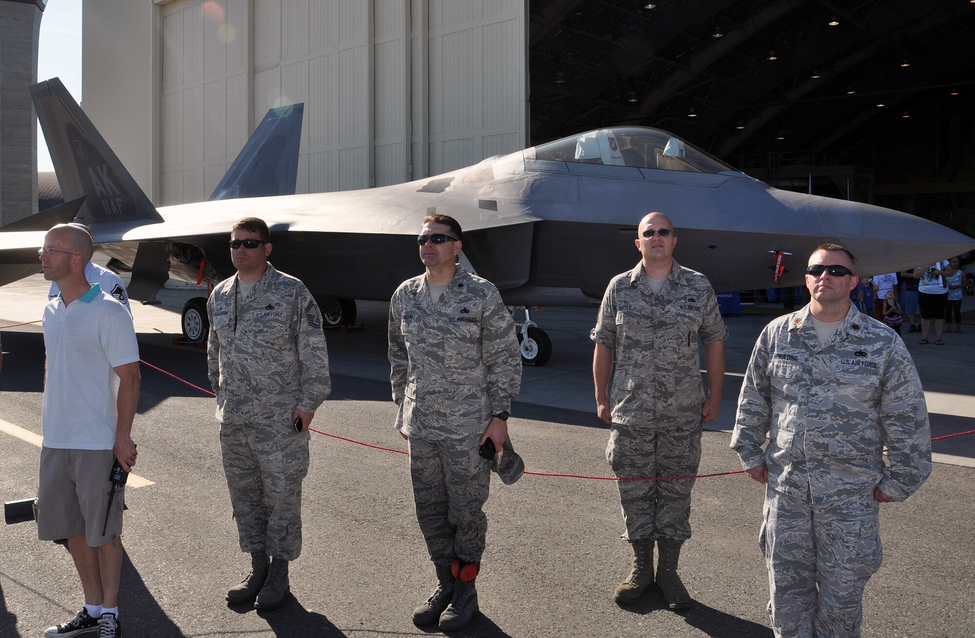 JOINT BASE ELMENDORF-RICHARDSON, Alaska. Members of the 477th Aircraft Maintenance Squadron stand at attention in front of an F-22 as the U.S. Army’s Golden Knights drop onto JBER with the American Flag proudly on display. The Golden Knights demonstration kicked off the 2012 Arctic Thunder Open House. (U.S. Air Force Photo/Tech. Sgt. Dana Rosso) 