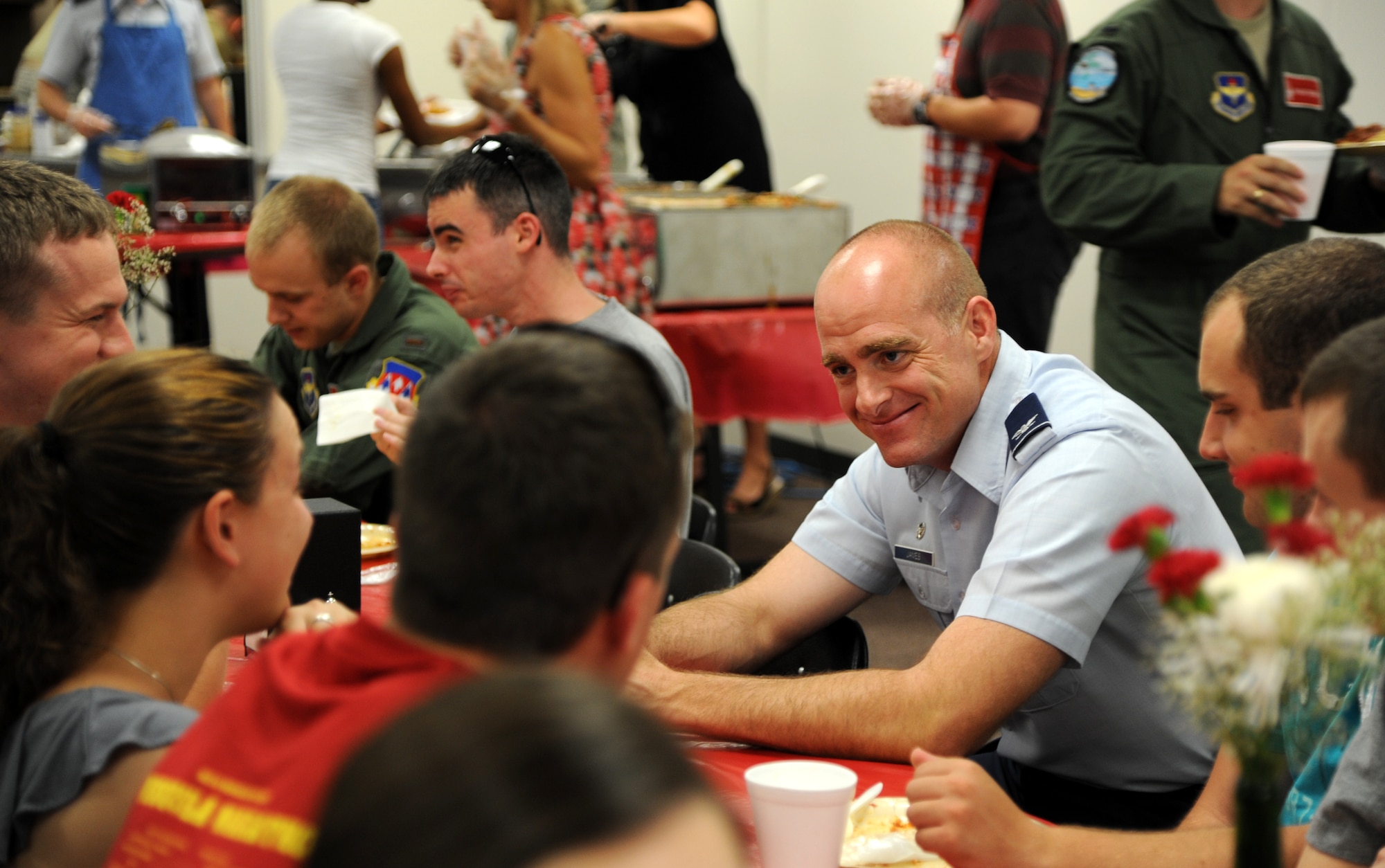 Col. Darren James, wearing light blue shirt, talks with Airmen and family members attending the July Singles’ International Gourmet Meal Opportunity held July 30 in the Community Chapel Activity Center at Vance Air Force Base, Okla. Colonel James, the 71st Flying Training Wing commander, helped serve Italian food to more than 180 diners. SIGMO is a free home-cooked meal offered monthly to single Airmen and the families of deployed Airmen at Vance AFB. (U.S. Air Force photo/ Airman 1st Class Frank Casciotta)