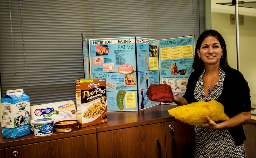 Wendy Wyatt, Health and Wellness Center dietician, compares five pounds of fat to five pounds of muscle. Behind Wyatt is a healthy eating display she uses when teaching nutritional classes. Wyatt is a registered dietician who recently joined the HAWC team. The HAWC’s mission is to cultivate a fit and healthy force. (U.S. Air Force photo by Senior Airman Dennis Sloan/Released)