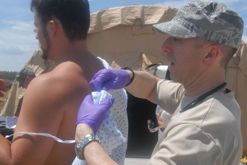 Maj. (Dr.) Michael Maine, a family practice doctor, helps a "patient" into a gown after he removed his clothing to prevent radiation particles from contanimating the hospital July 28 during Vibrant Response 13. (DoD photo by Army Sgt. 1st Class Raymond J. Piper)