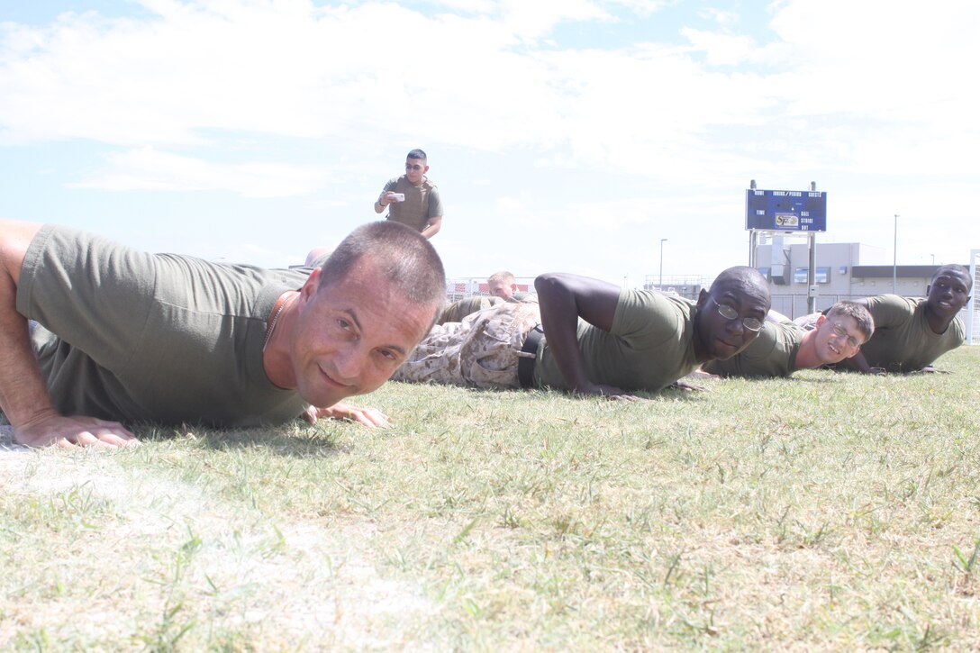 (From Left to Right) Maj. Frederick L. Lewis, Headquarters and Headquarters Squadron commanding officer, Master Sgt. Lionel Saulsberry, station postal chief, Lance Cpl. Frank M. Pikula, a station judge advocate legal service specialist, and Lance Cpl. Kayvon A. Blount, a station postal clerk, wait poised to perform a pushup and then play tug-of-war at the H&HS field meet at Penny Lake Fields here Aug. 1, 2012. H&HS Headquarters department, Provost Marshal’s Office, station operations and station logistics competed in the field meet. PMO won overall. The field meet was composed of seven events: Arm-wrestling, the Dizzy Izzy, a relay race, pugil stick striking, a Humvee pull, tug-of-war and Own-the Bone.