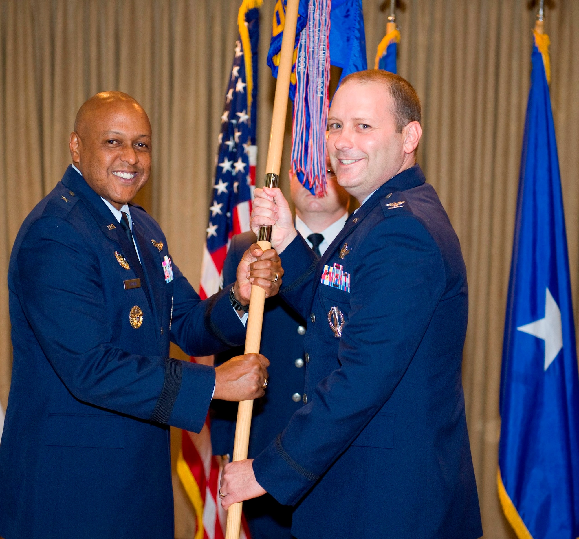 Brig. Gen. Anthony Cotton, left, commander, 45th Space Wing, passes the unit guidon to Col. Douglas Schiess during the Operations Group Change of Command ceremony Monday at the Tides. Col. Schiess is succeeding Col. Denette Sleeth. In the background is Chief Master Sgt James Isom of the 45th Operations Group. (Photo by Julie Dayringer)