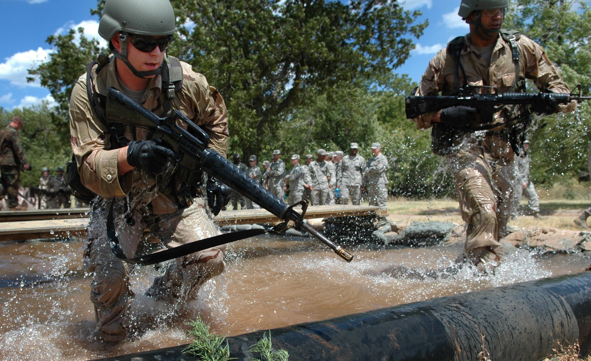 As fellow members of the 3rd Combat Communications Group look on, Staff Sgt. Jason Schad, 33rd Combat Communications Squadron, left, and Tech. Sgt. John Rucker, 3rd Combat Communications Support Squadron, leap up from defensive positions in the water and prepare to move on to the next obstacle of the Individual Movements Course with their fire team. (Air Force photo by Micah Garbarino)