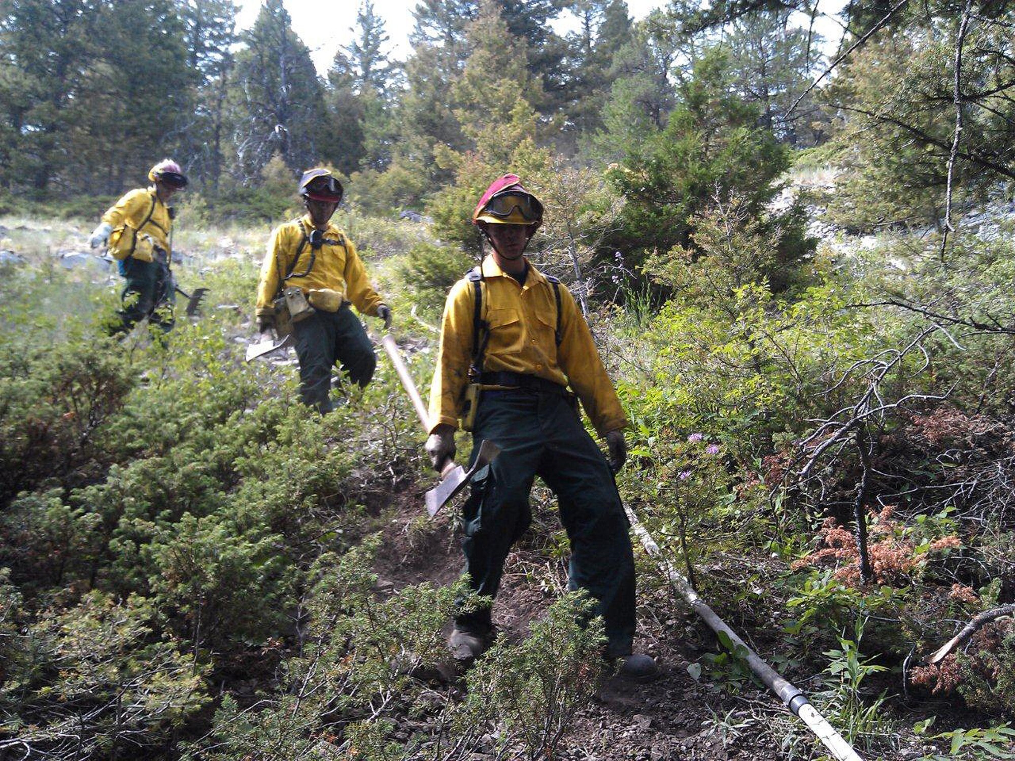 From left to right: 341st Civil Engineer Squadron fire department Staff Sgts. David Rogan, Robert Lysholm and Juan Hernandez hike through rough terrain on a steep hill to get to the perimeter of the fire.  Several Malmstrom firemen responded to a wild land fire alongside local fire departments, following a Mutual Aid request on July 22.  (U.S. Air Force courtesy photo)