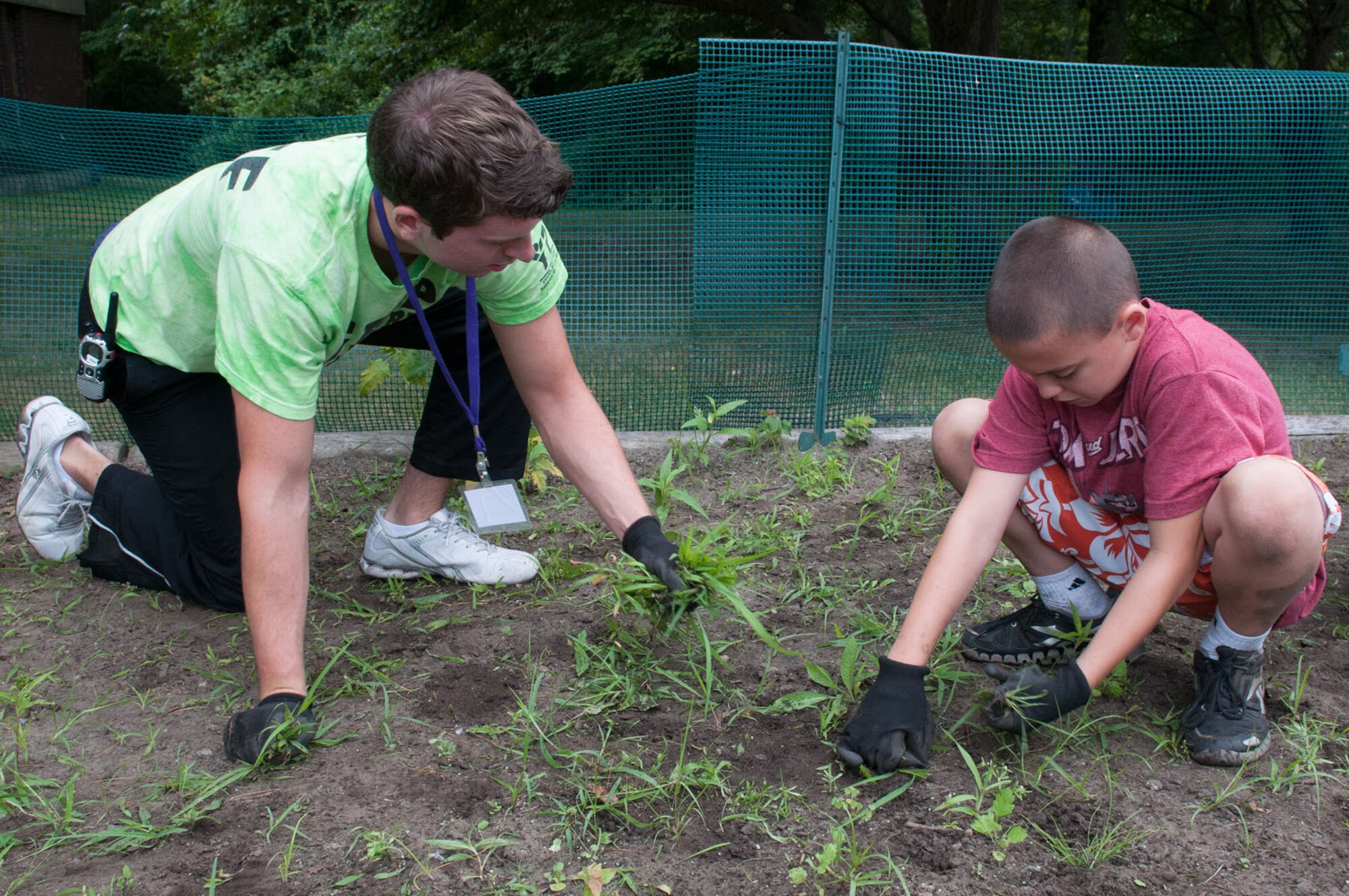HANSCOM AIR FORCE BASE, Mass. - Drew Haughn, Camp Adventure staff member, and Dylan Franzoni, camper, pull weeds in the community garden near the Youth Center July 26. The junior counselors and campers pull weeds to allow the planted flowers, vegetables and herbs to grow better in the garden. (U.S. Air Force photo by Rick Berry)