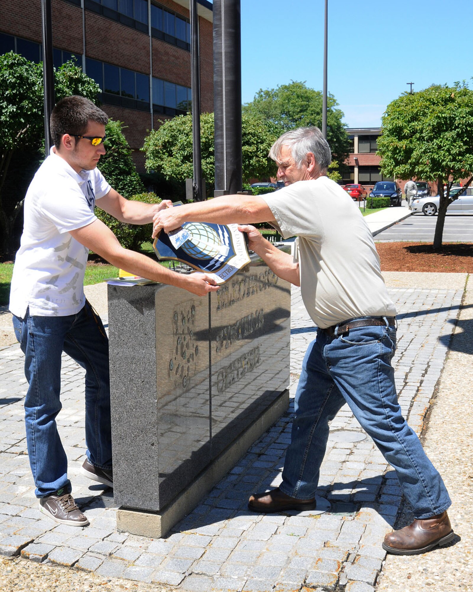 HANSCOM AIR FORCE BASE , Mass. - Bob Peach, a structures supervisor, hands the old Electronic Systems Center shield to Jesse Leister, an intern with Civil Engineering, as he removes it from the granite sign in front of Building 1606 July 25. ESC officially became part of the Air Force Life Cycle Management Center during a transition ceremony July 16. (U.S. Air Force photo by Linda LaBonte Britt)