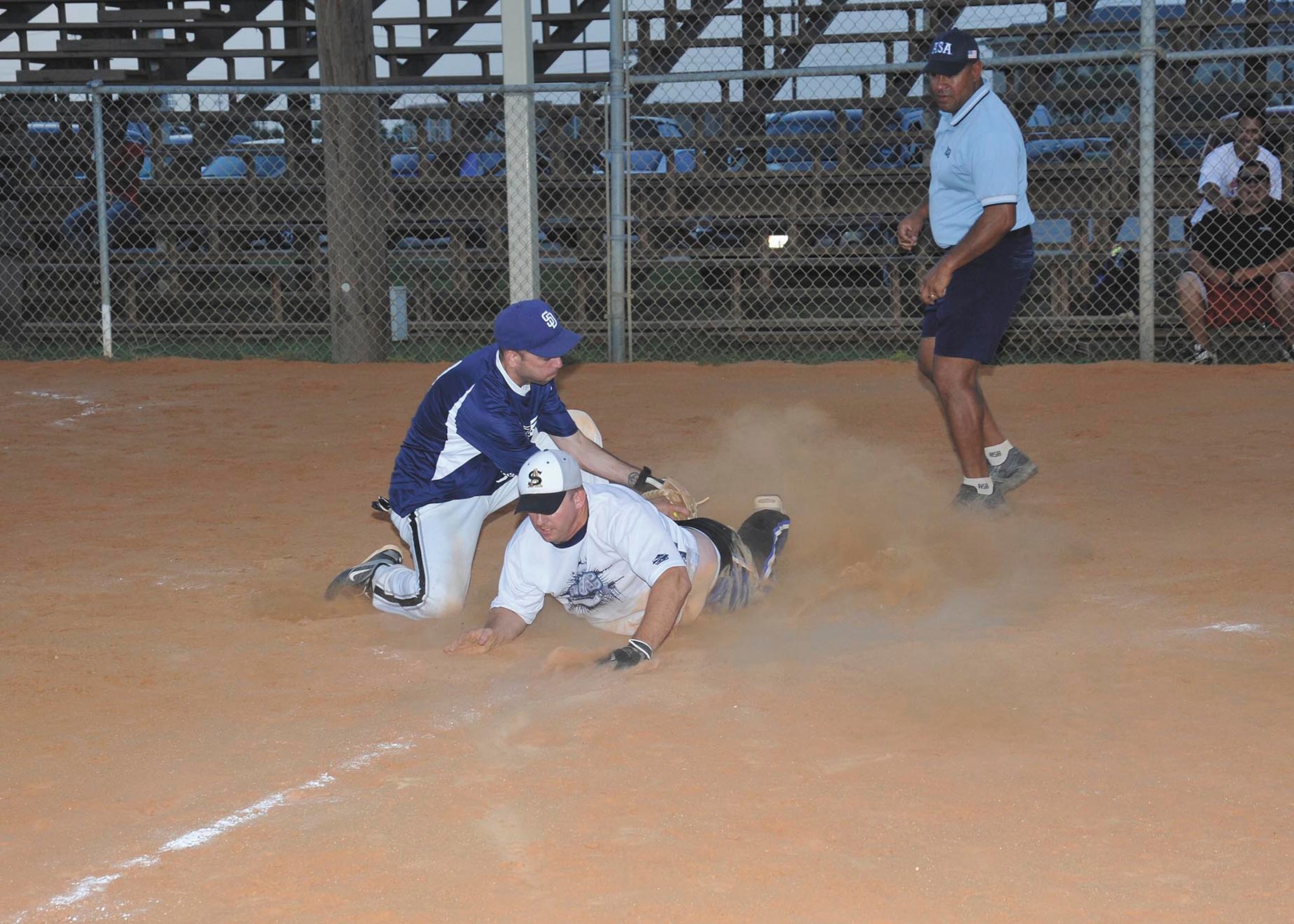 Navy Information Operations Command-Texas base runner Ross Beebe slides under the tag as 343rd Training Squadron catcher James Bice tries to take him out at home July 26 during the Joint Base San Antonio-Lackland intramural softball tournament championship game. Home plate umpire Jesse Jenkins called Beebe safe. NIOC-Texas, and the 343rd TRS will join the 802nd Force Support Squadron and the 624th Operations Center at the all-JBSA intramural softball tournament, which begins Monday at JBSA-Randolph. (U.S. Air Force photo/Alan Boedeker)